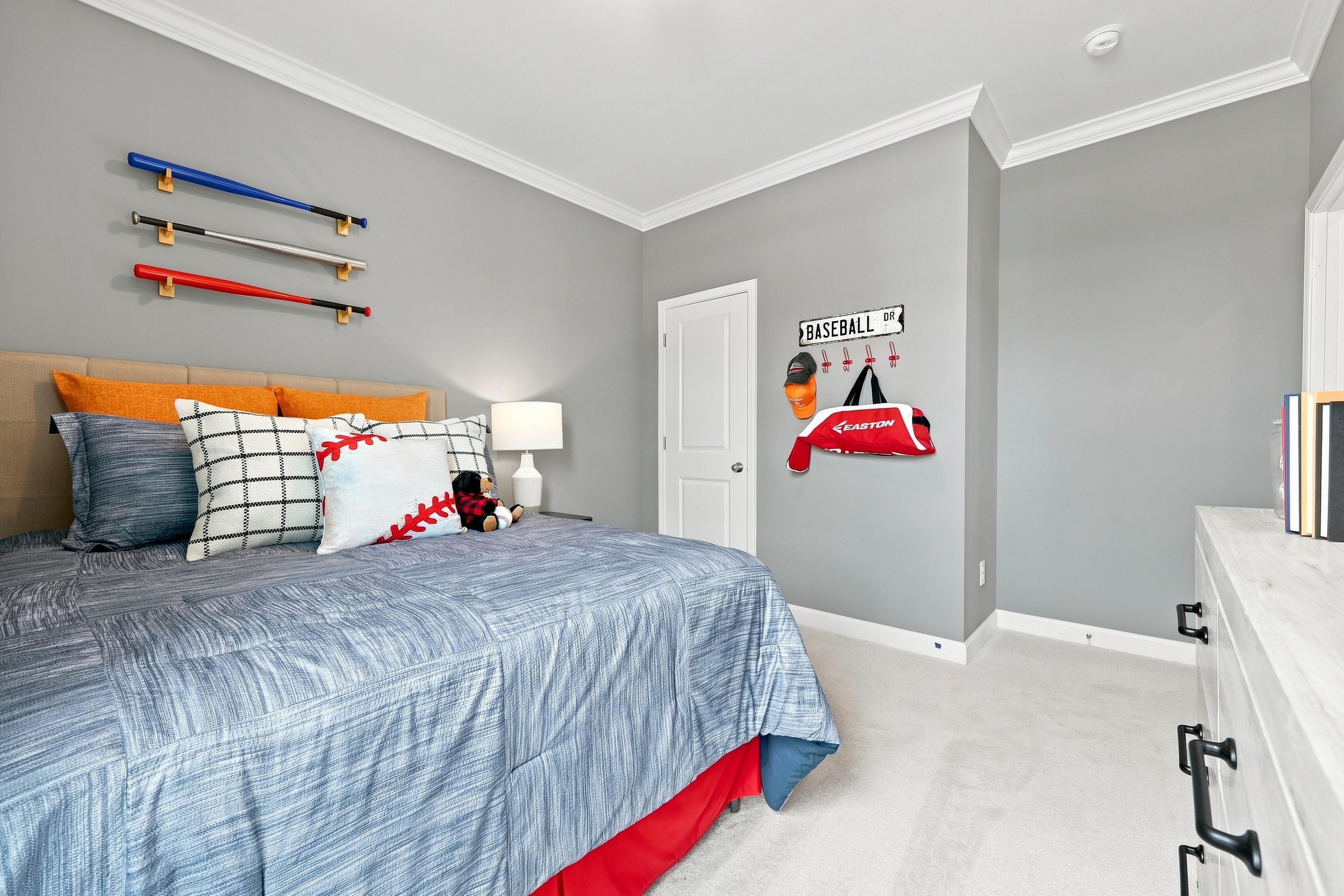 Baseball-themed bedroom in The Daphne D home design featuring a sport-inspired decor, bedding, and wall-mounted bats.