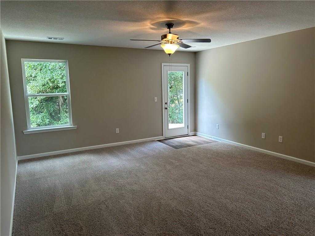 Spacious living room with beige walls, carpet flooring, ceiling fan, large windows, and sliding patio door in Davidson Homes The Washington, Phenix City