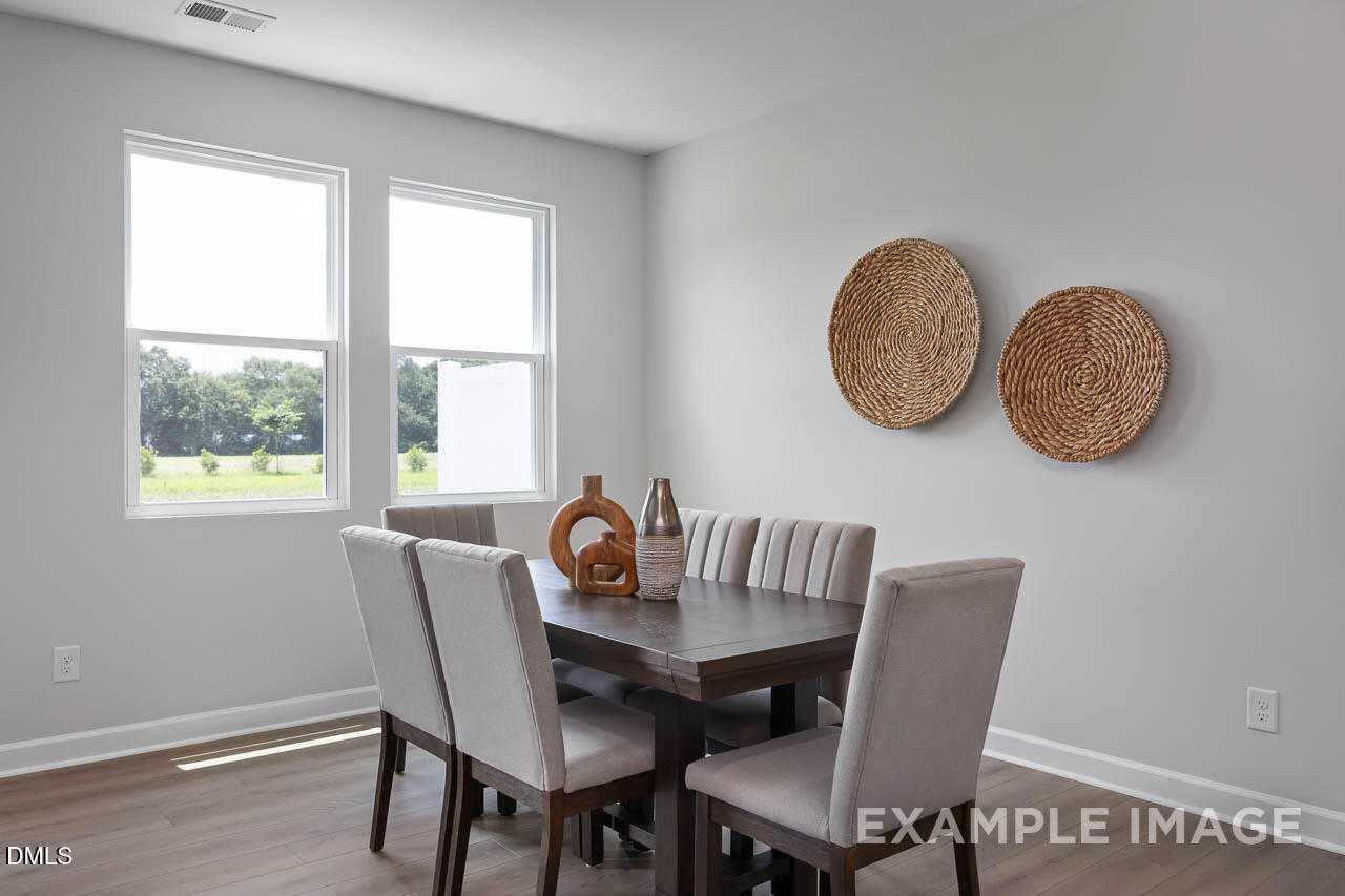 Elegant dining room featuring wooden table, upholstered chairs, woven wall baskets, and natural light in The Warren floor plan, Fuquay-Varina, NC