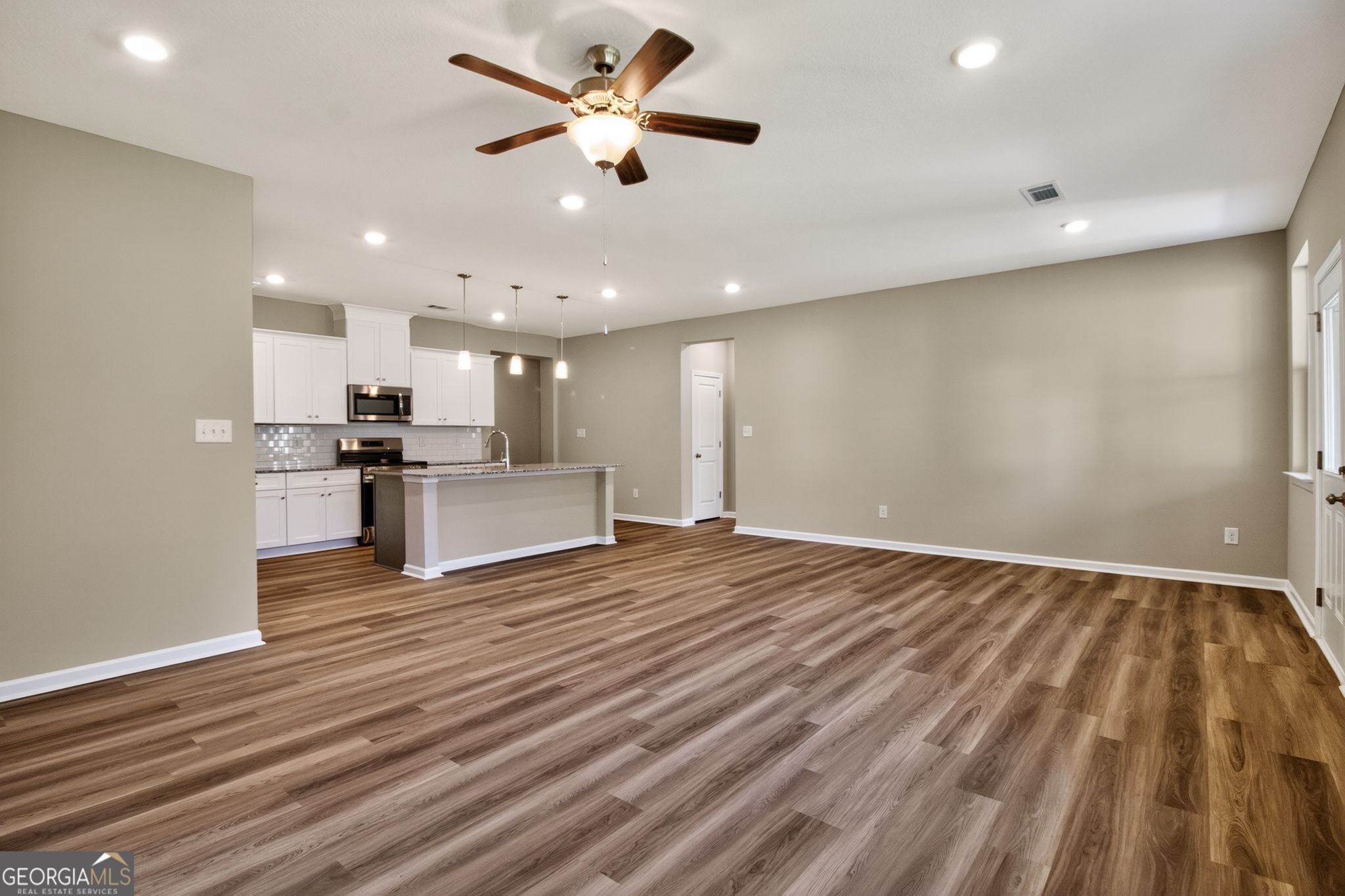 Open-concept kitchen and living area with hardwood floors, white cabinets, stainless appliances, and ceiling fans in 4-bedroom The Luna home, Perry, Georgia