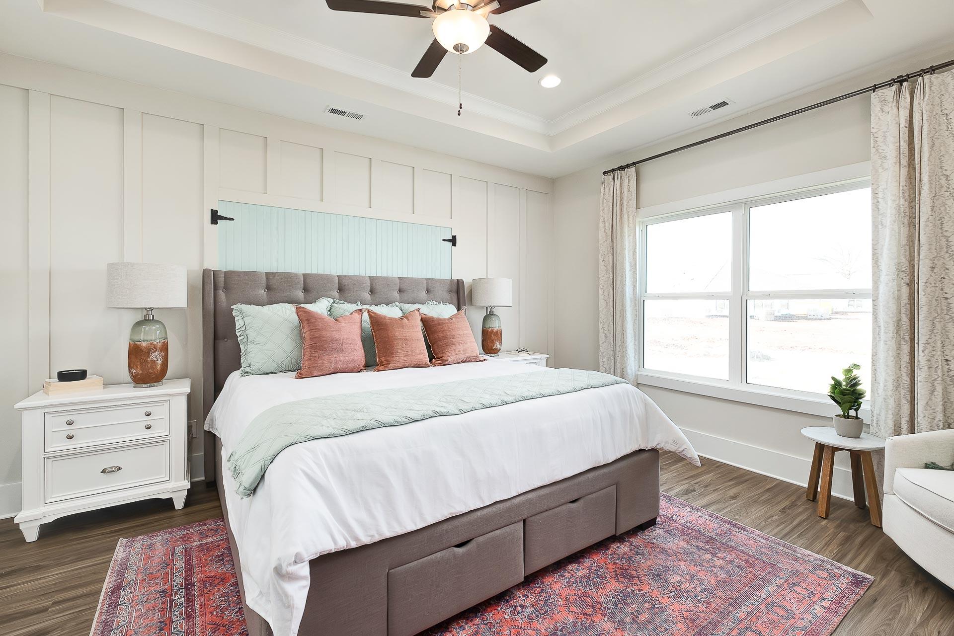 Spacious primary bedroom at Newby Chapel in Athens AL with tufted gray headboard, ceiling fan, hardwood floors, and large windows