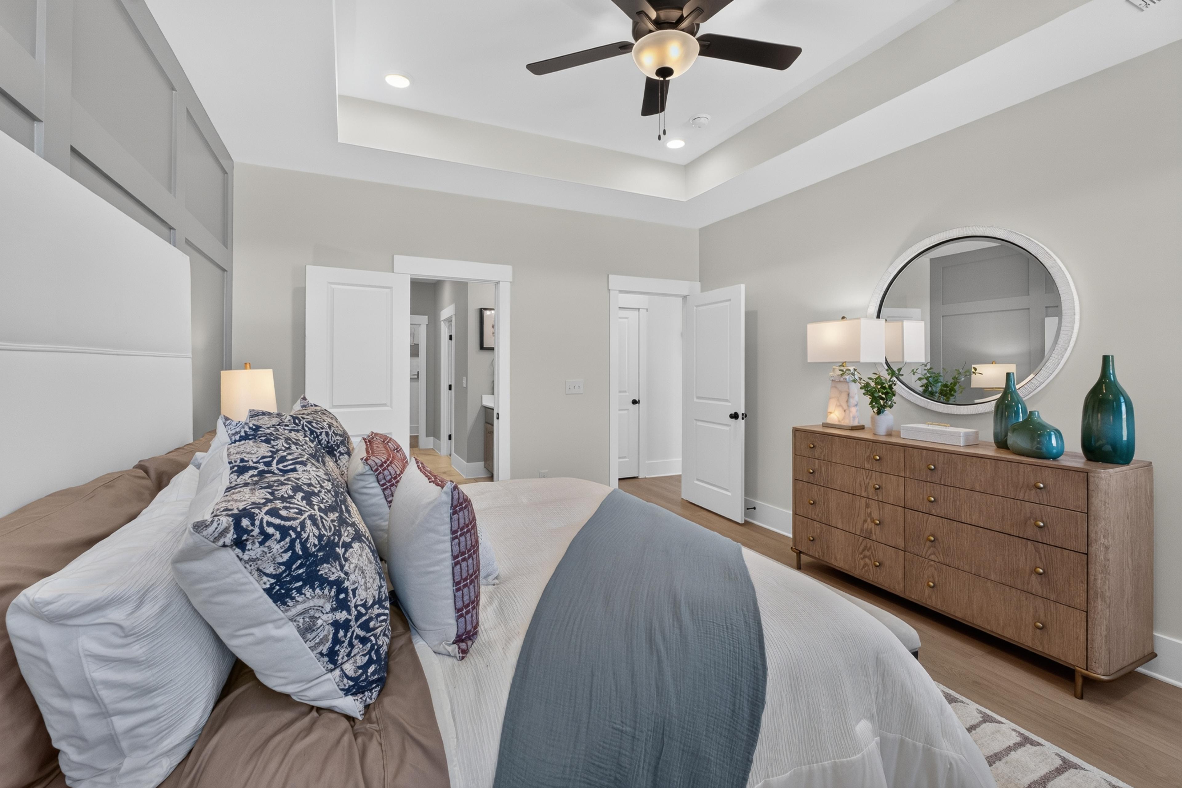 Bright primary bedroom at Evergreen Mill in Madison, AL with tray ceiling, ceiling fan, and wood dresser by Davidson Homes