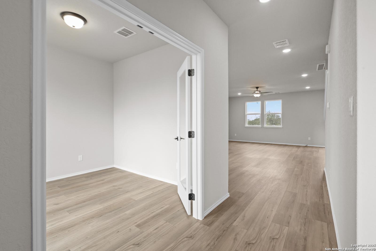 Bright home office with open door to spacious living area, wood laminate floors, ceiling fan in Davidson Homes Murray J, San Antonio