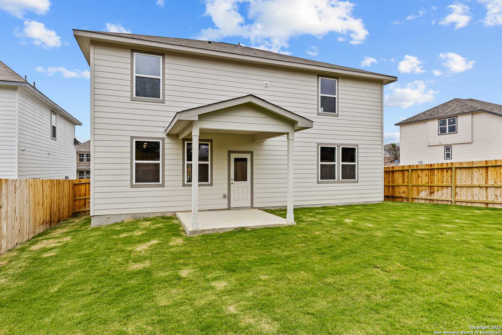 Back view of two-story Davidson Homes Douglas F with covered patio, wooden fence, and lush grassy yard in Royal Crest, San Antonio, Texas