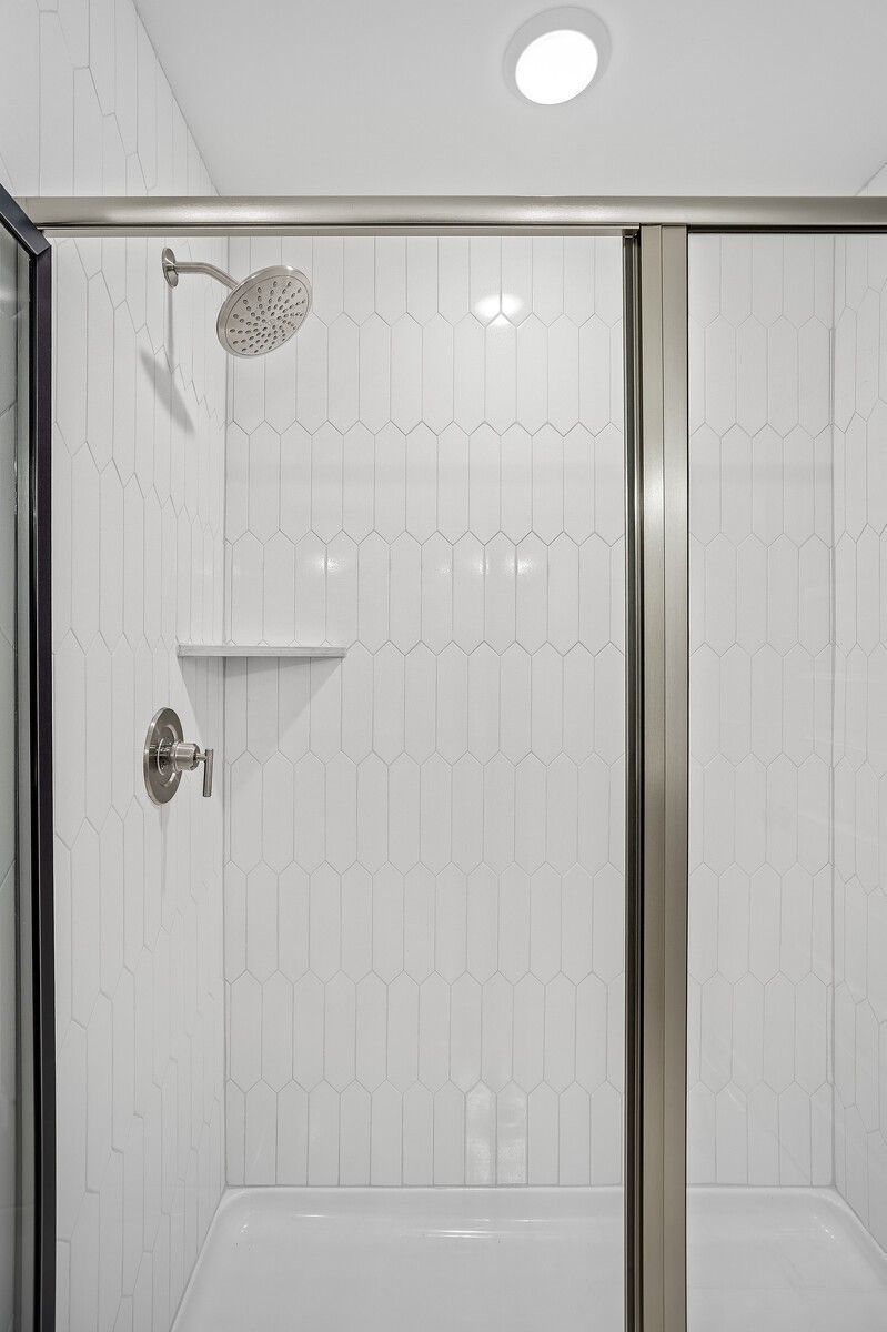 Modern frameless glass shower with white subway tile walls, herringbone floor, and rainfall showerhead in Davidson Homes The Logan C, Gallatin, TN