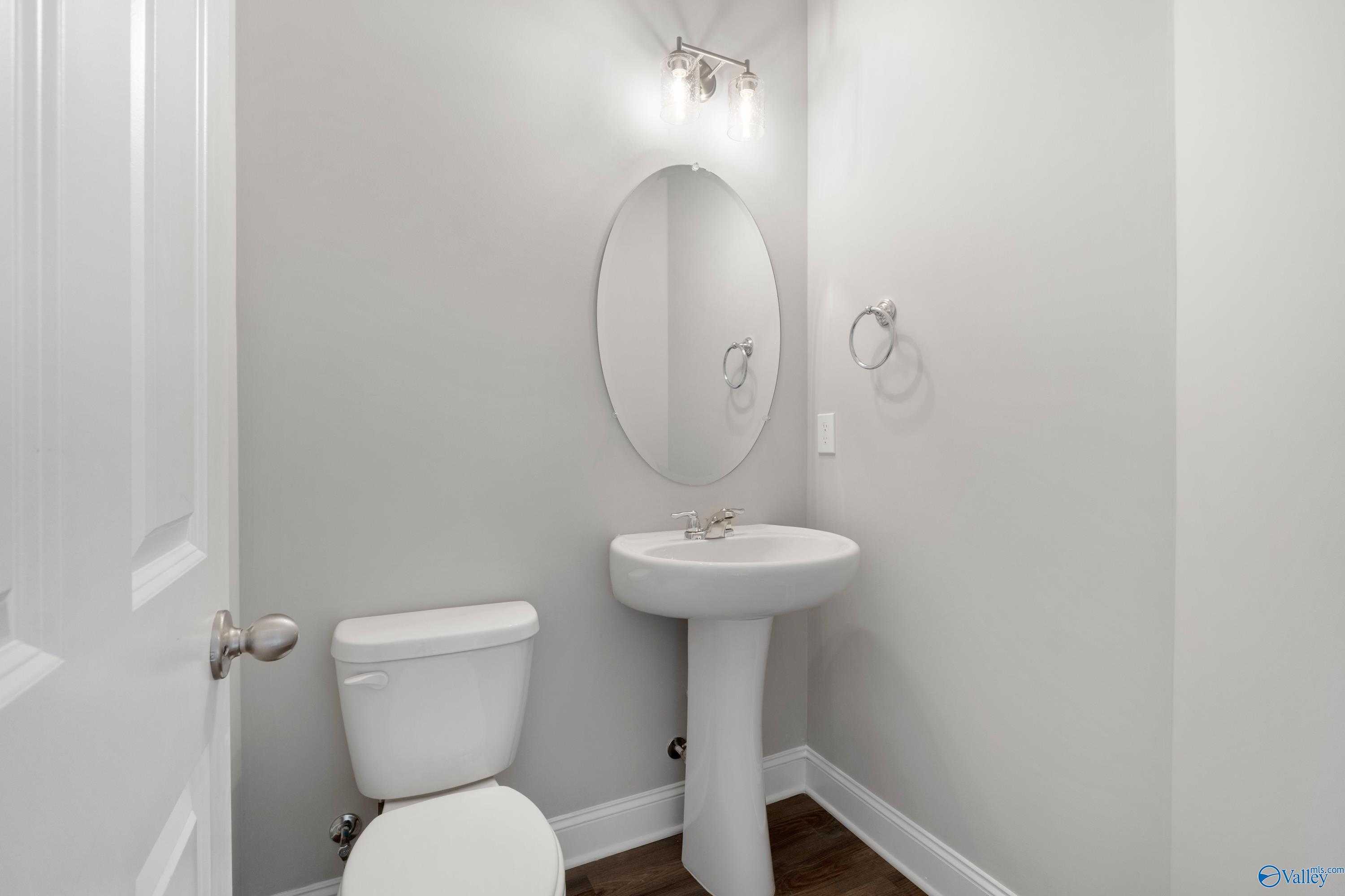Elegant powder room featuring pedestal sink, round mirror, and wall sconce in Davidson Homes The Aiken, Meridianville, Alabama