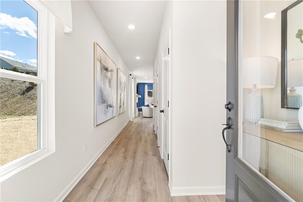 Bright hallway with hardwood floors, white walls, abstract artwork, and scenic window view in Davidson Homes The Burton C, Canton, Georgia