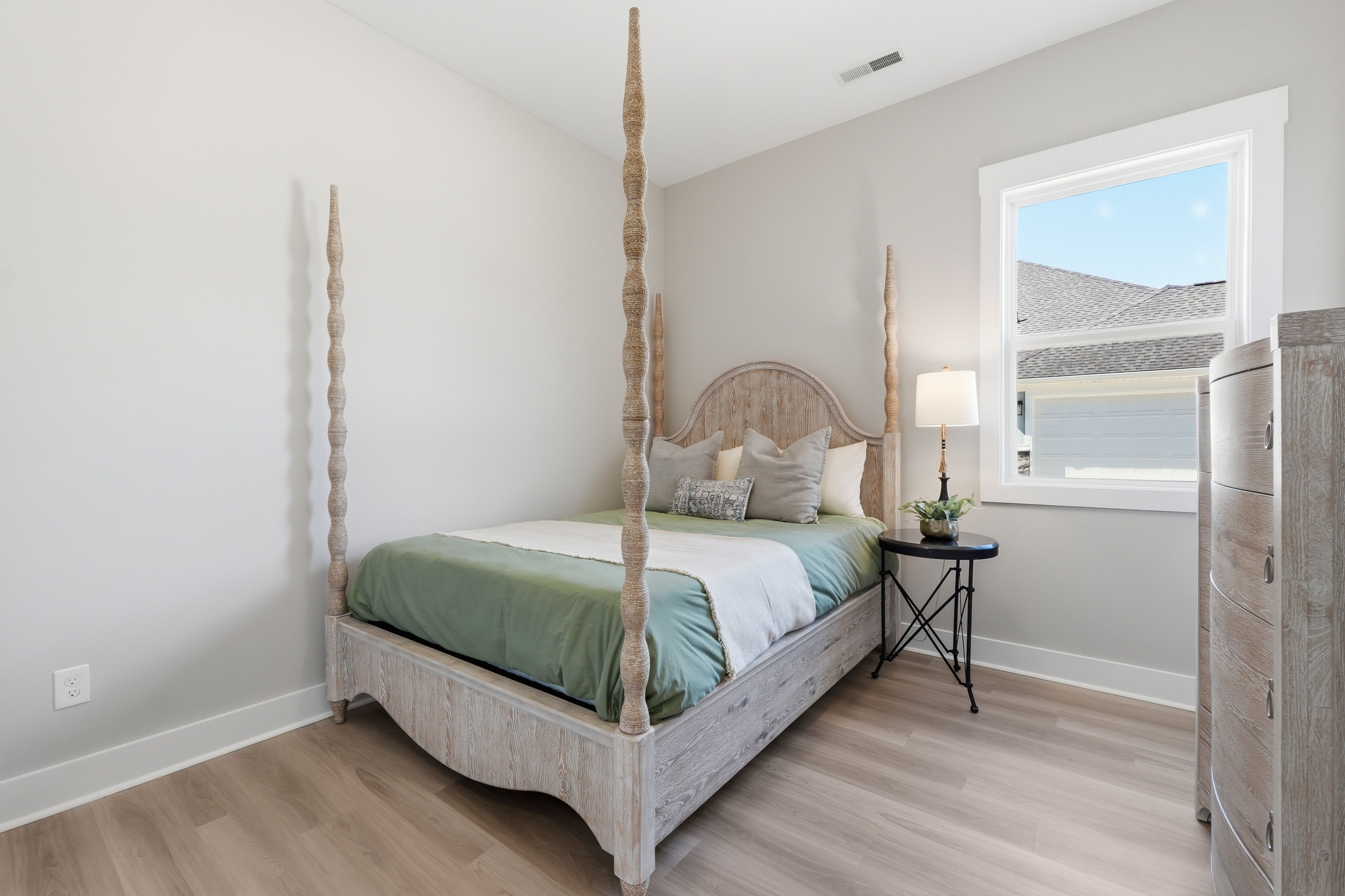 Spacious bedroom with white four-poster bed, green linens, nightstand lamp, and window view in The Meadows at Hampton Cove, Owens Cross Roads AL