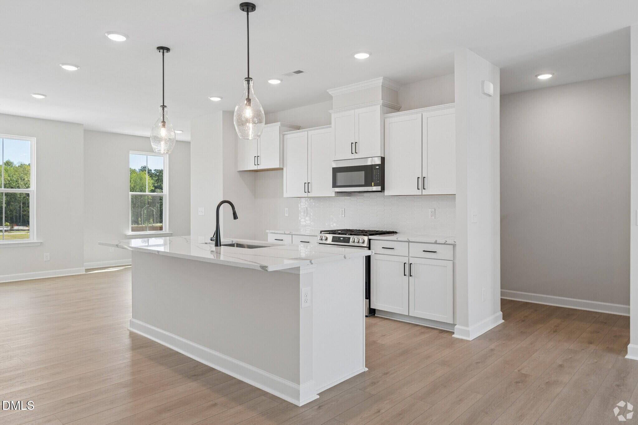 Bright open-concept kitchen with white shaker cabinets, quartz island, and stainless appliances in The Mitchell plan, Knightdale NC