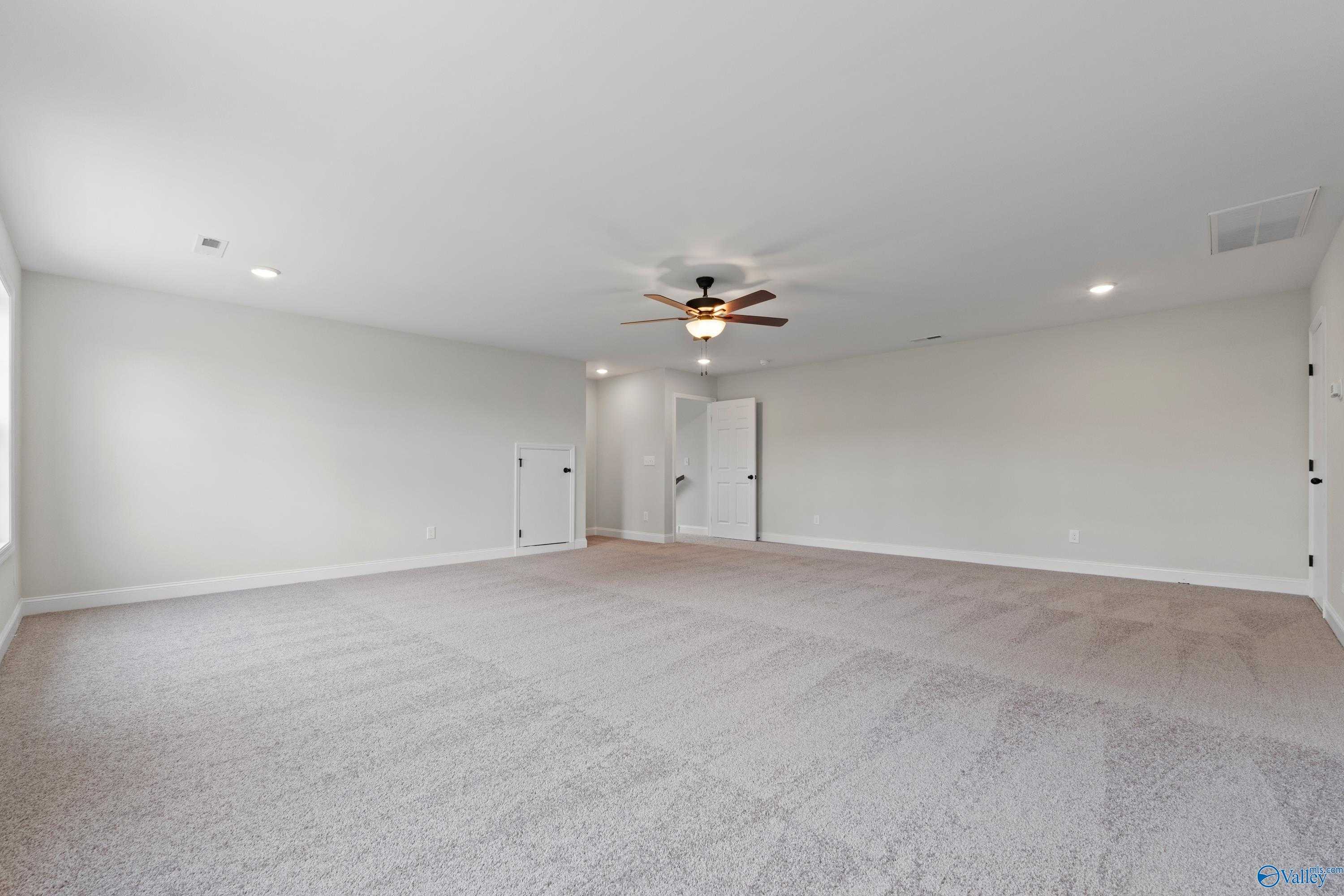 Spacious bonus room featuring ceiling fan, beige carpet, and double doors in Davidson Homes The Kirkland with Bonus, Harvest, AL