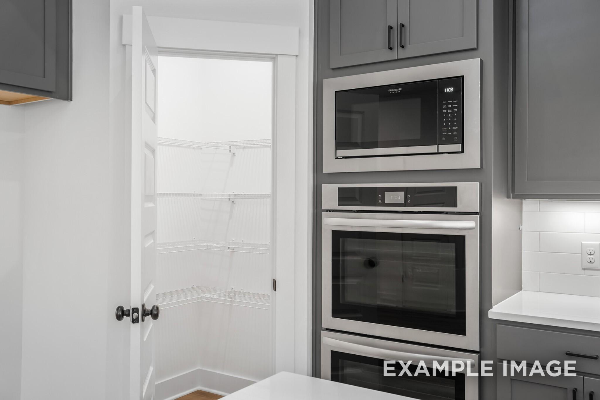 Modern kitchen with open walk-in pantry, stainless microwave, double wall oven, and gray shaker cabinets in Davidson Homes Ridgeport C, Gallatin, TN