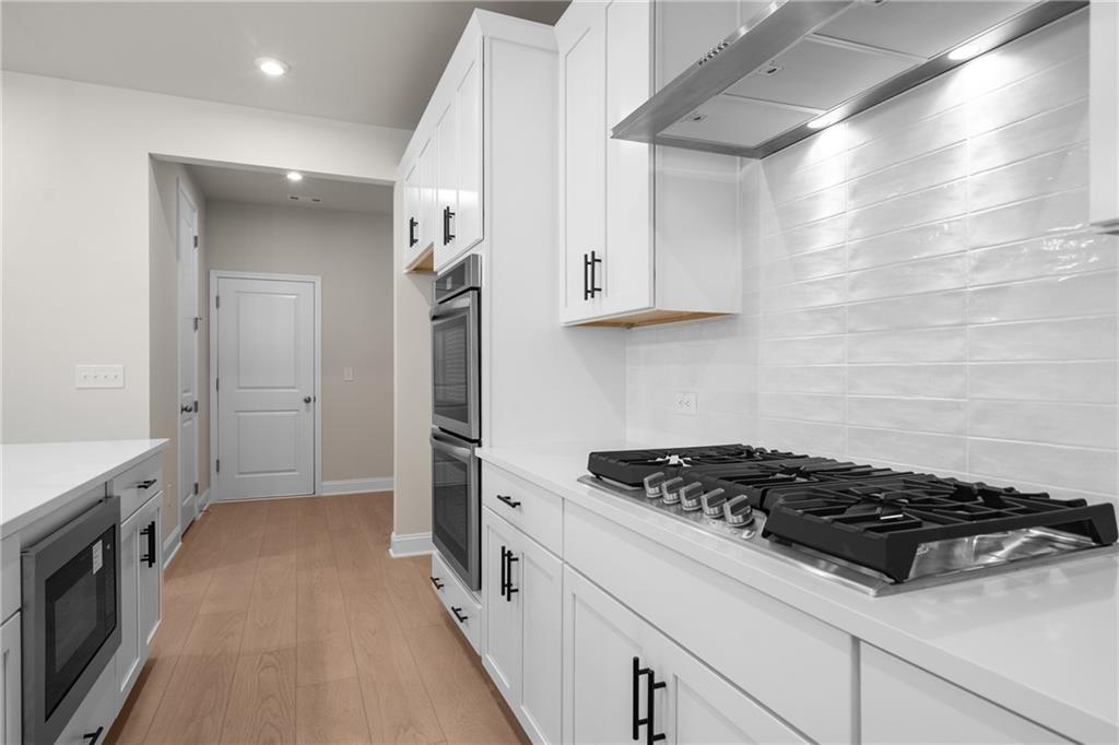 Modern white kitchen with shaker cabinets, stainless gas range, double ovens, and island microwave in The Hickory E, Buford, Georgia