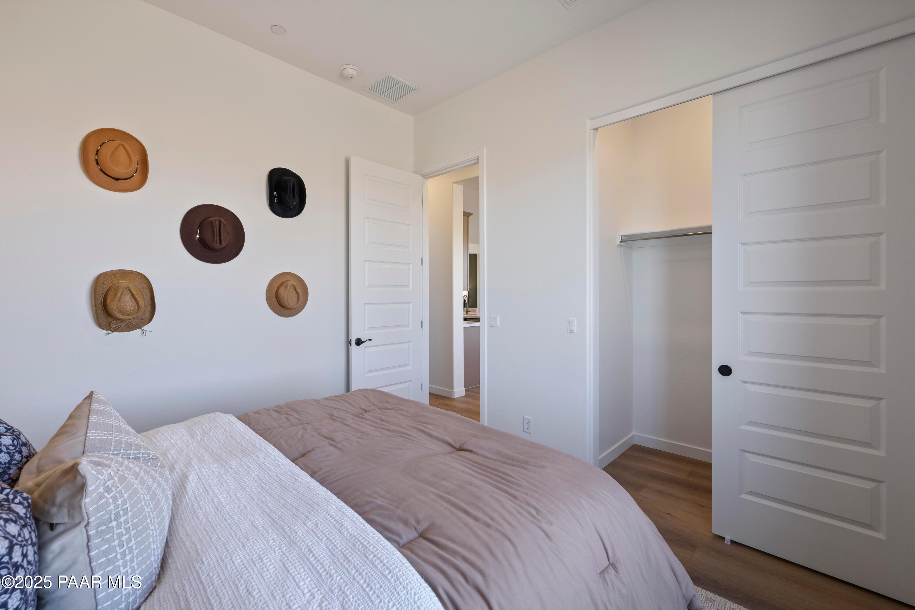 Cozy bedroom with cowboy hats on wall, neutral bedding on bed, sliding closet doors, and open bathroom entry in Davidson Homes The Blaze D, Prescott AZ