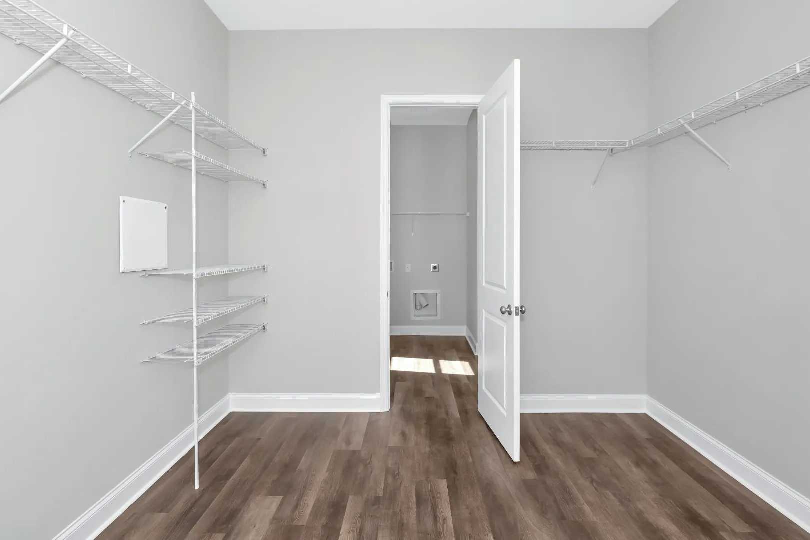 Spacious walk-in closet in The Arcadia M master suite featuring white shelving, gray walls, wood floors, open door to laundry