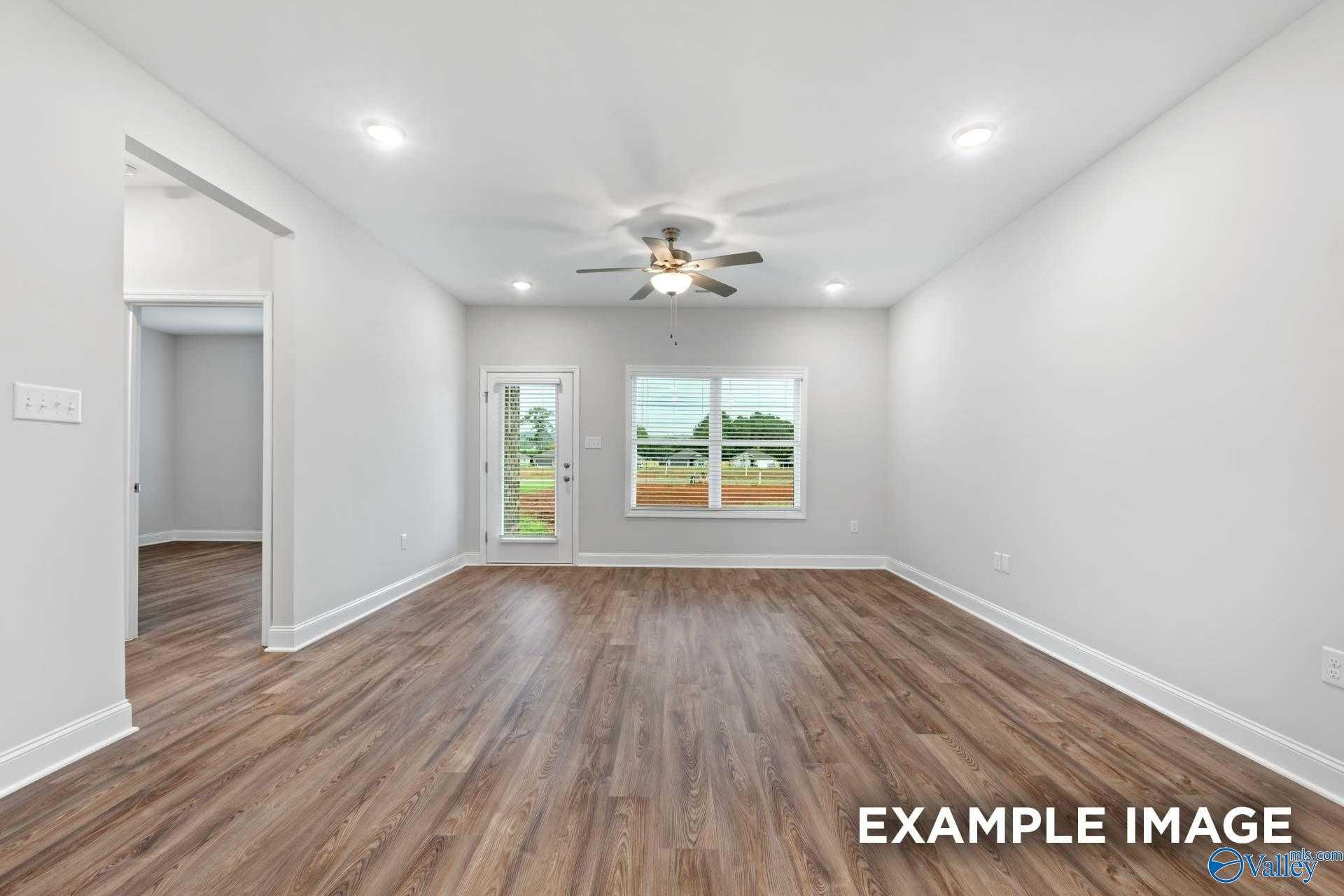 Bright living room with hardwood floors, ceiling fan, and large windows overlooking yard in Davidson Homes The Cumberland, Decatur, Alabama