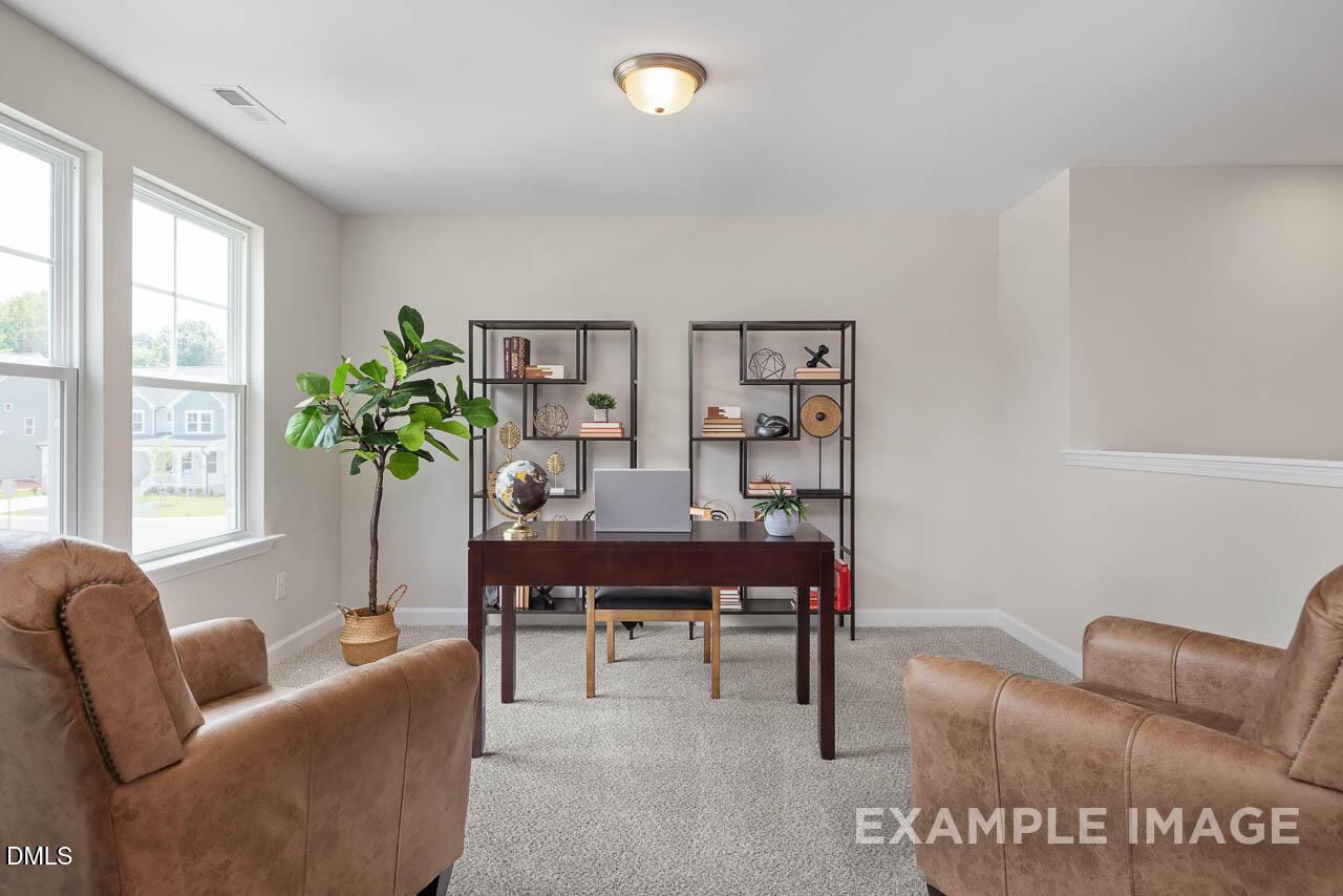 Cozy home office with wooden desk, leather armchairs, fiddle leaf fig, and bookshelves in Davidson Homes The Willow D, Lillington NC