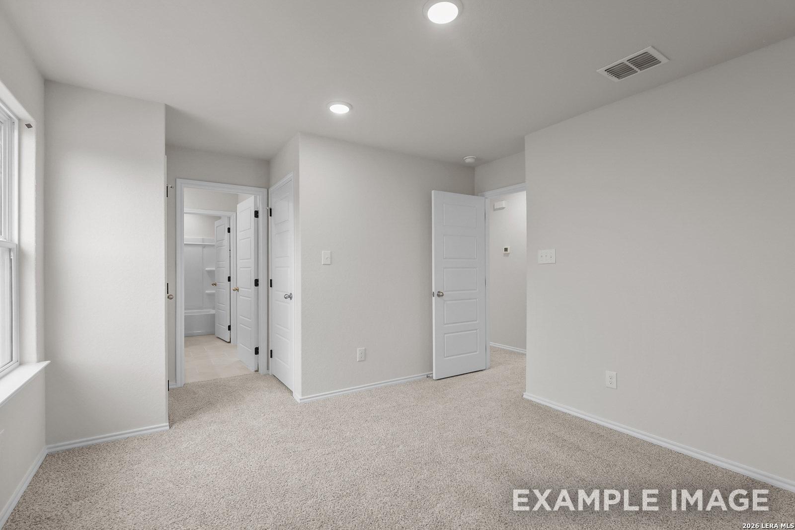 Spacious bedroom with carpeted flooring and adjacent en suite bathroom in The Sequoia C plan, Royal Crest, San Antonio.