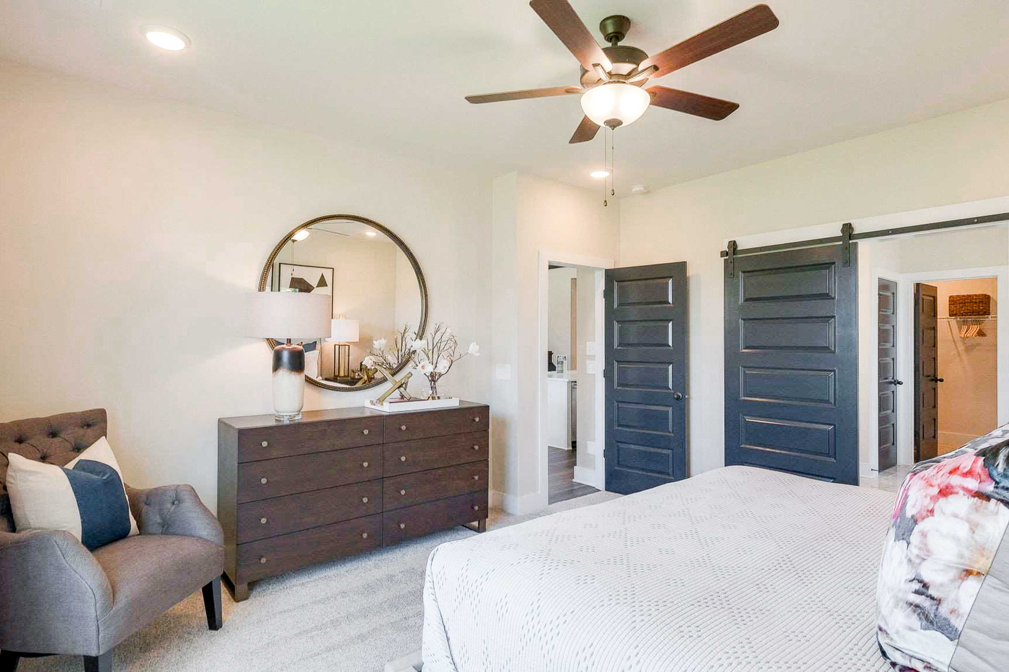 Spacious master bedroom at The Meadows in Smyrna TN featuring barn doors, ceiling fan, and tufted armchair