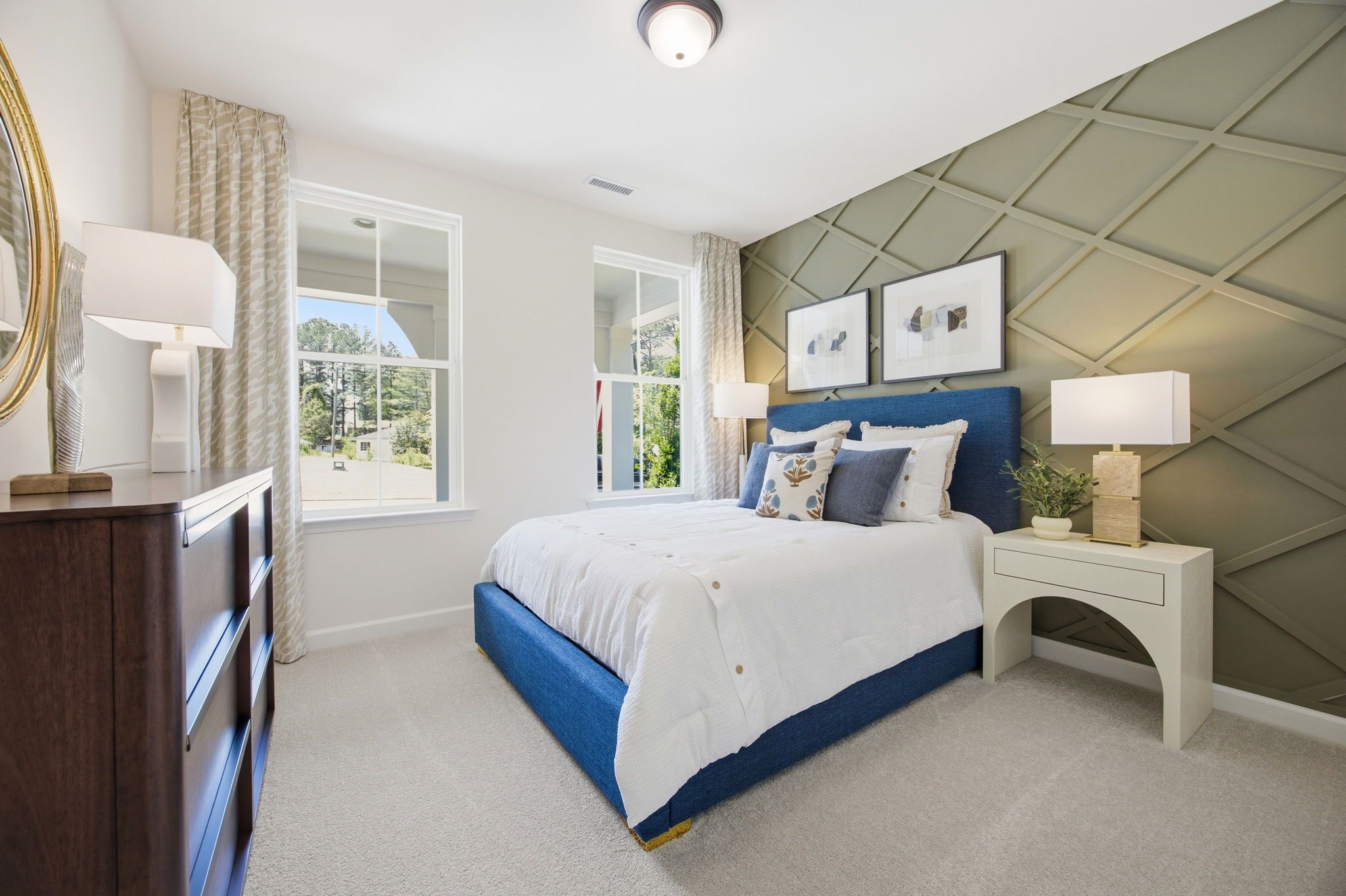Spacious bedroom at Sage on North Main in Wake Forest NC with blue upholstered bed, sage green diamond accent wall, and tree-view windows