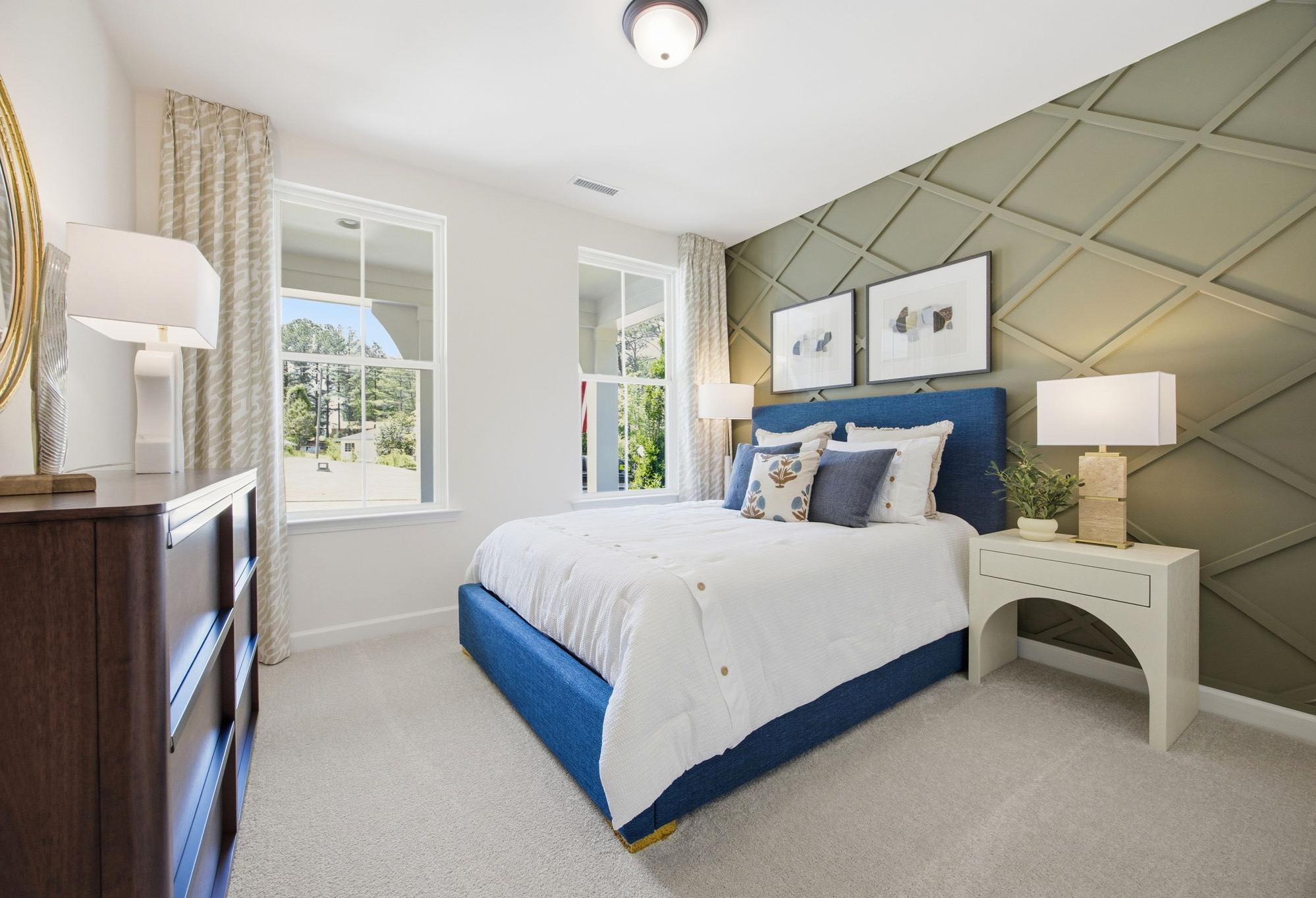 Master suite bedroom in The Ashport G featuring a blue upholstered bed and stylish olive green accent wall with molding.