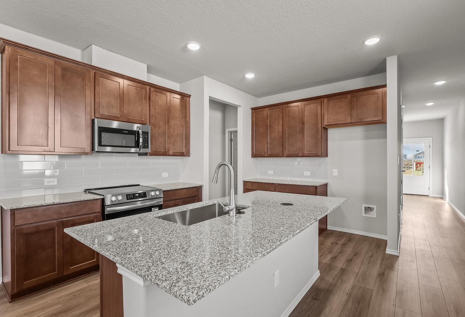 Modern kitchen in The Arroyo featuring granite countertops, wood cabinetry, and a spacious center island.