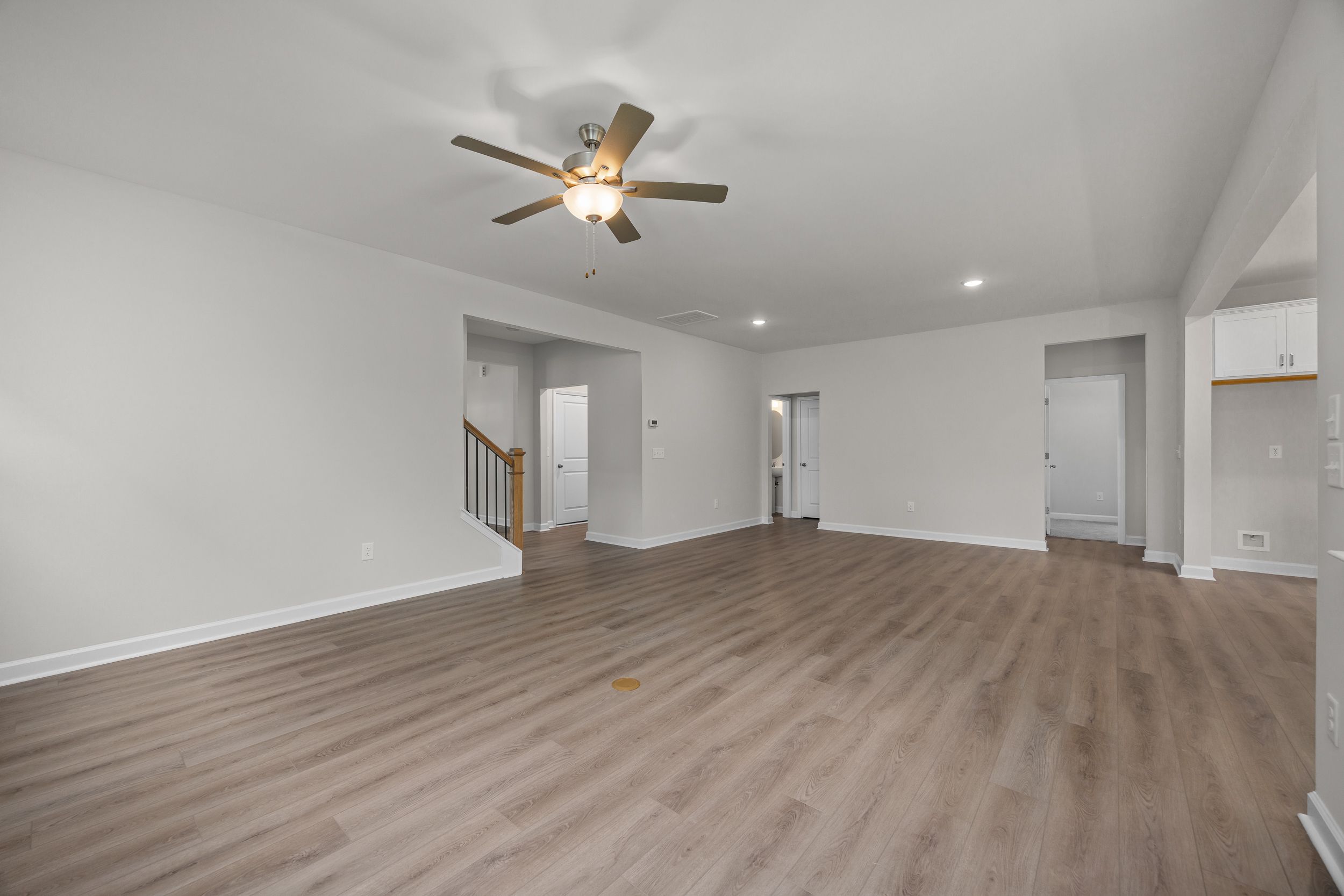 Spacious open-concept living area in The Aspen Davidson Homes with light hardwood floors, white walls, ceiling fan, and staircase