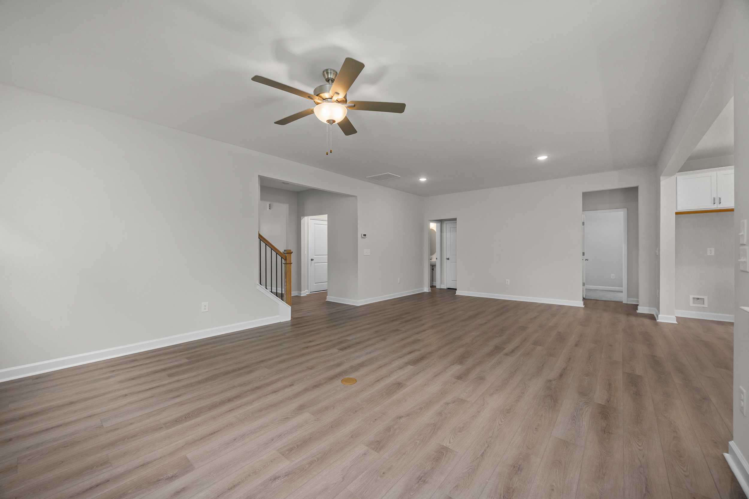 Spacious open-concept living area in The Aspen Davidson Homes with light hardwood floors, white walls, ceiling fan, and staircase
