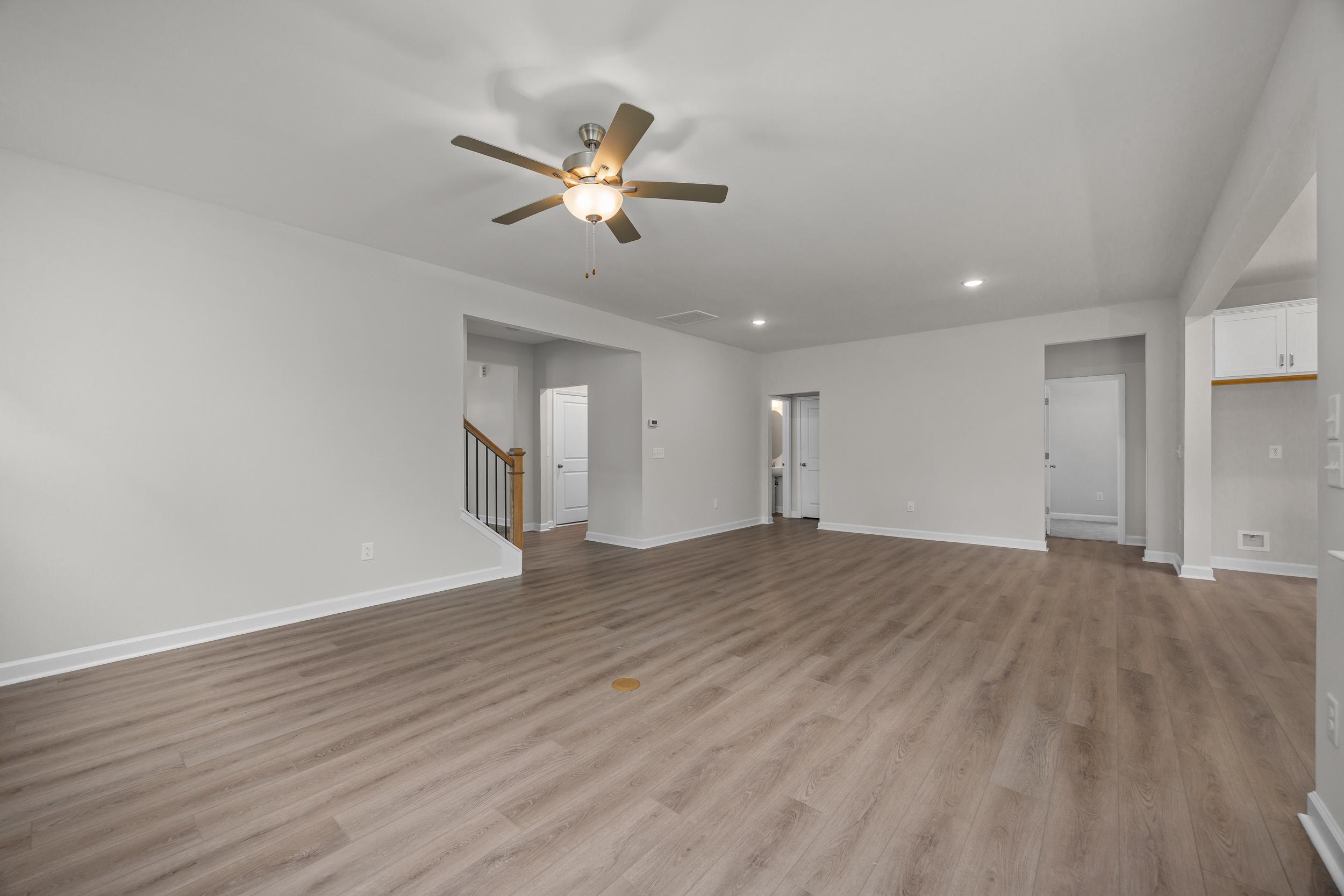 Spacious open-concept living area in The Aspen Davidson Homes with light hardwood floors, white walls, ceiling fan, and staircase