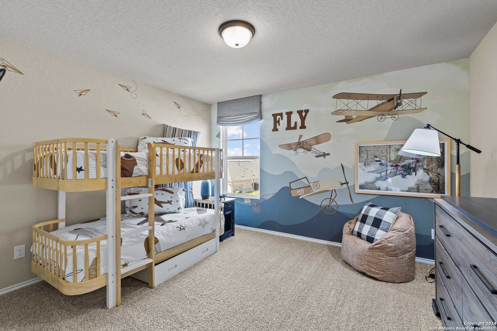 Aviation-themed kids' bedroom with wooden bunk beds, airplane mural, and bean bag chair in Davidson Homes The Douglas F, Bricewood, San Antonio