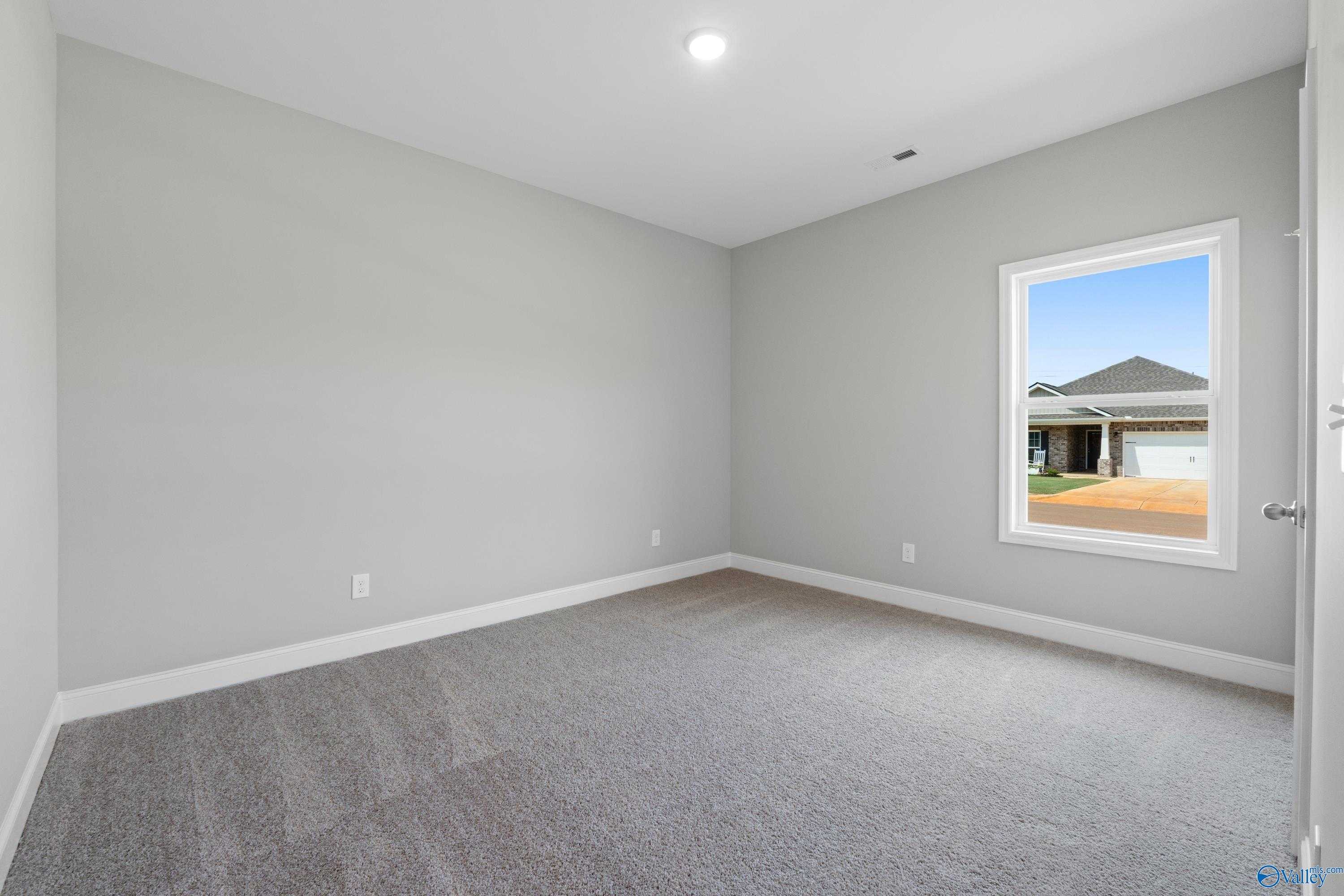 Empty bedroom with light gray walls, beige carpet, and large window overlooking backyard in Davidson Homes The Daphne C, Athens, Alabama
