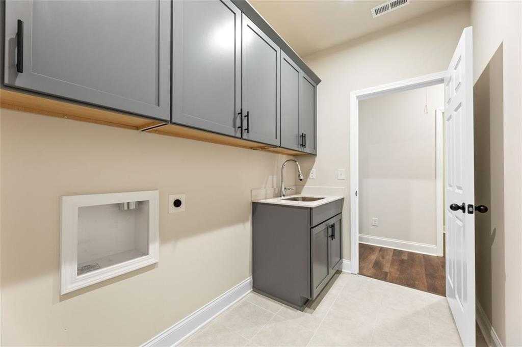 Modern laundry room with gray shaker cabinets, utility sink, and washer/dryer alcove in The Harrison G home, Hoschton, Georgia