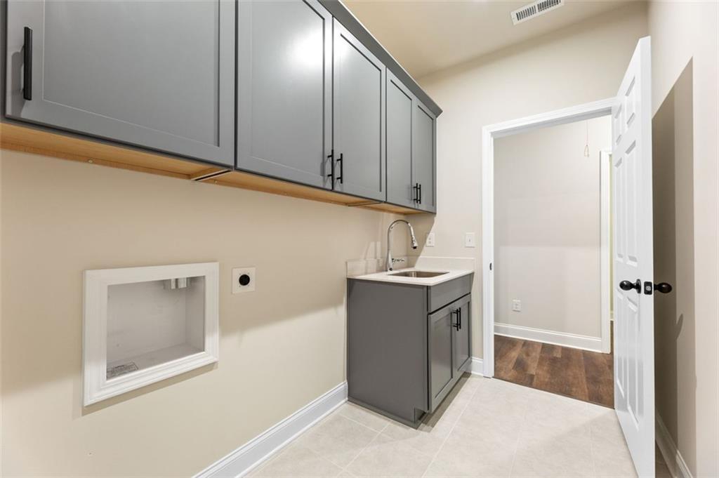 Modern laundry room featuring gray shaker cabinets, deep utility sink, and storage in Davidson Homes The Harrison G, Hoschton, GA