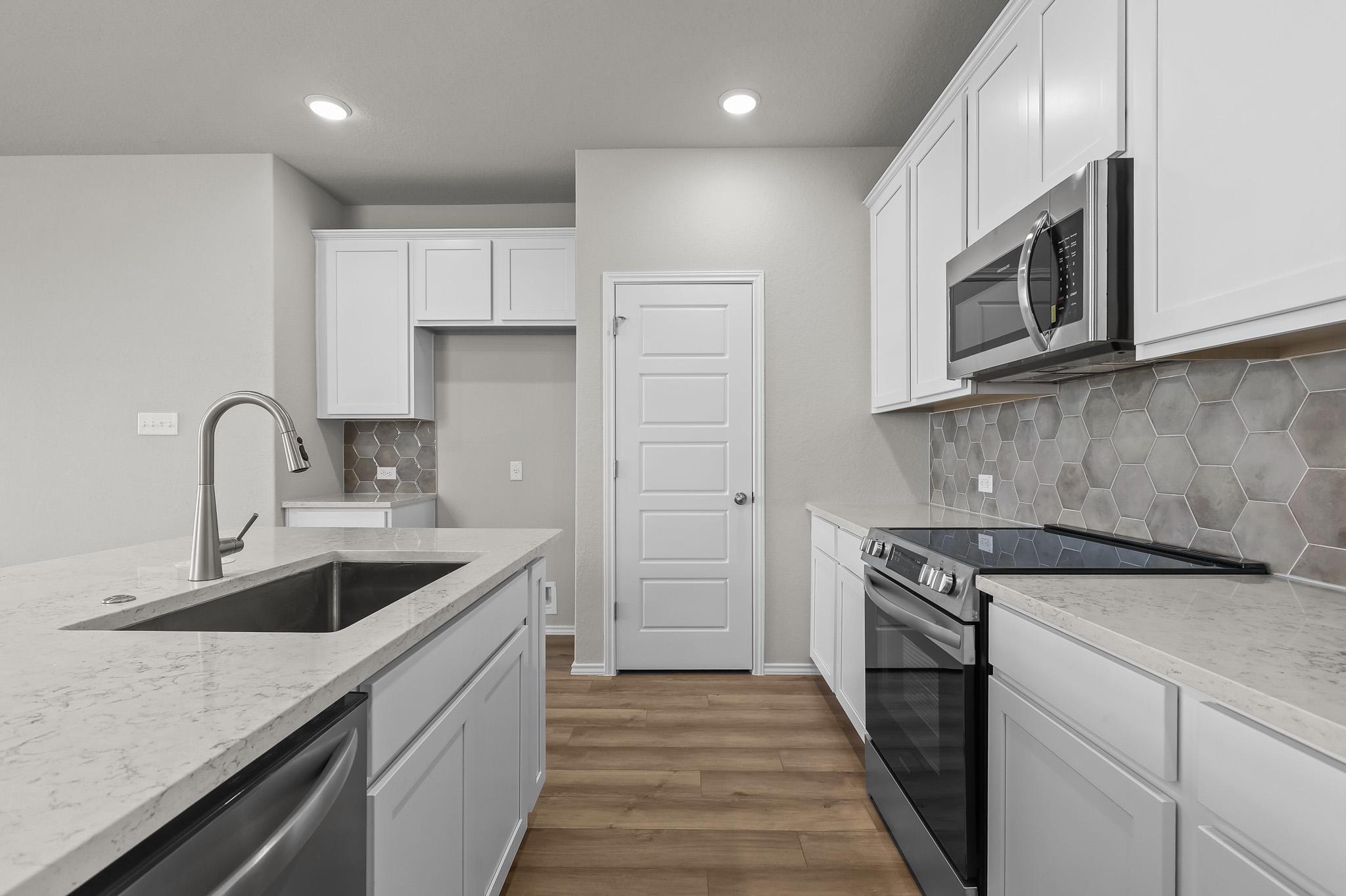 Modern kitchen in The Colorado B featuring white cabinets, quartz countertops, stainless steel appliances, and tile backsplash.