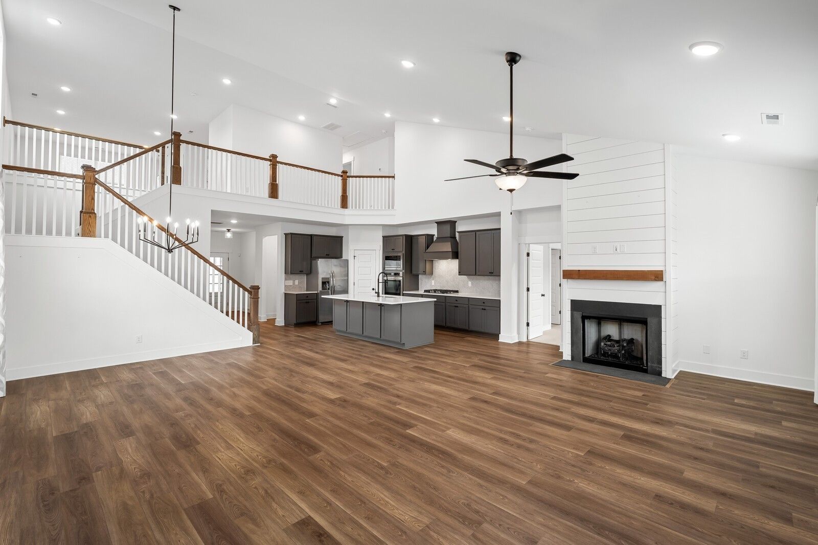Open two-story great room with shiplap accents, hardwood floors, kitchen island, staircase, and fireplace in Davidson Homes Ridgeport, Gallatin, TN