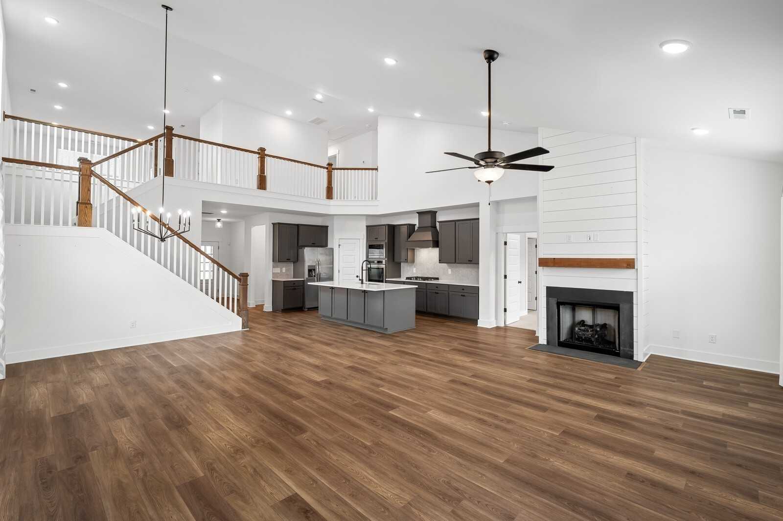 Open two-story great room with shiplap accents, hardwood floors, kitchen island, staircase, and fireplace in Davidson Homes Ridgeport, Gallatin, TN