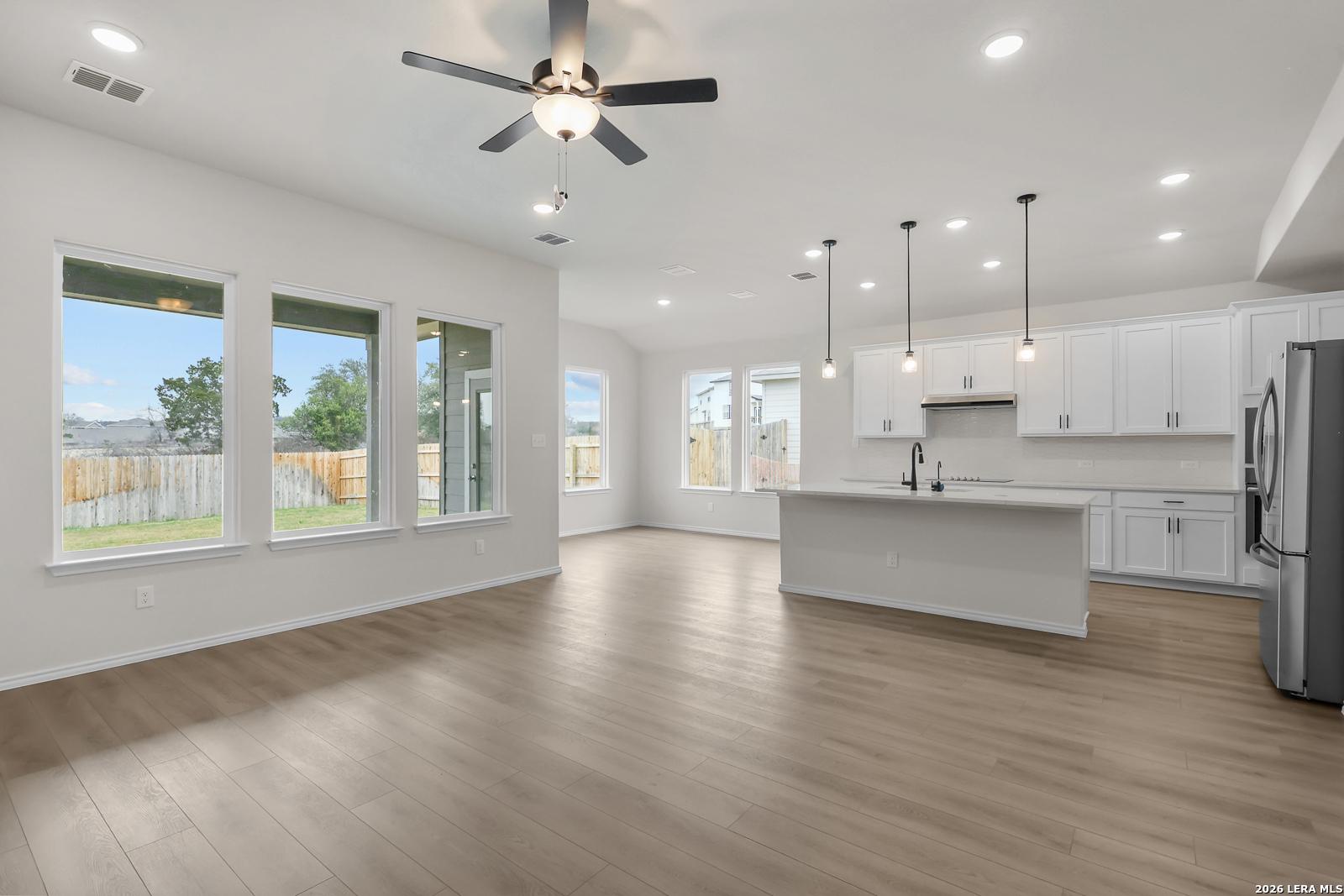 Modern open-concept kitchen with white cabinets, stainless fridge, island, ceiling fans, and backyard view in The Sequoia A, San Antonio