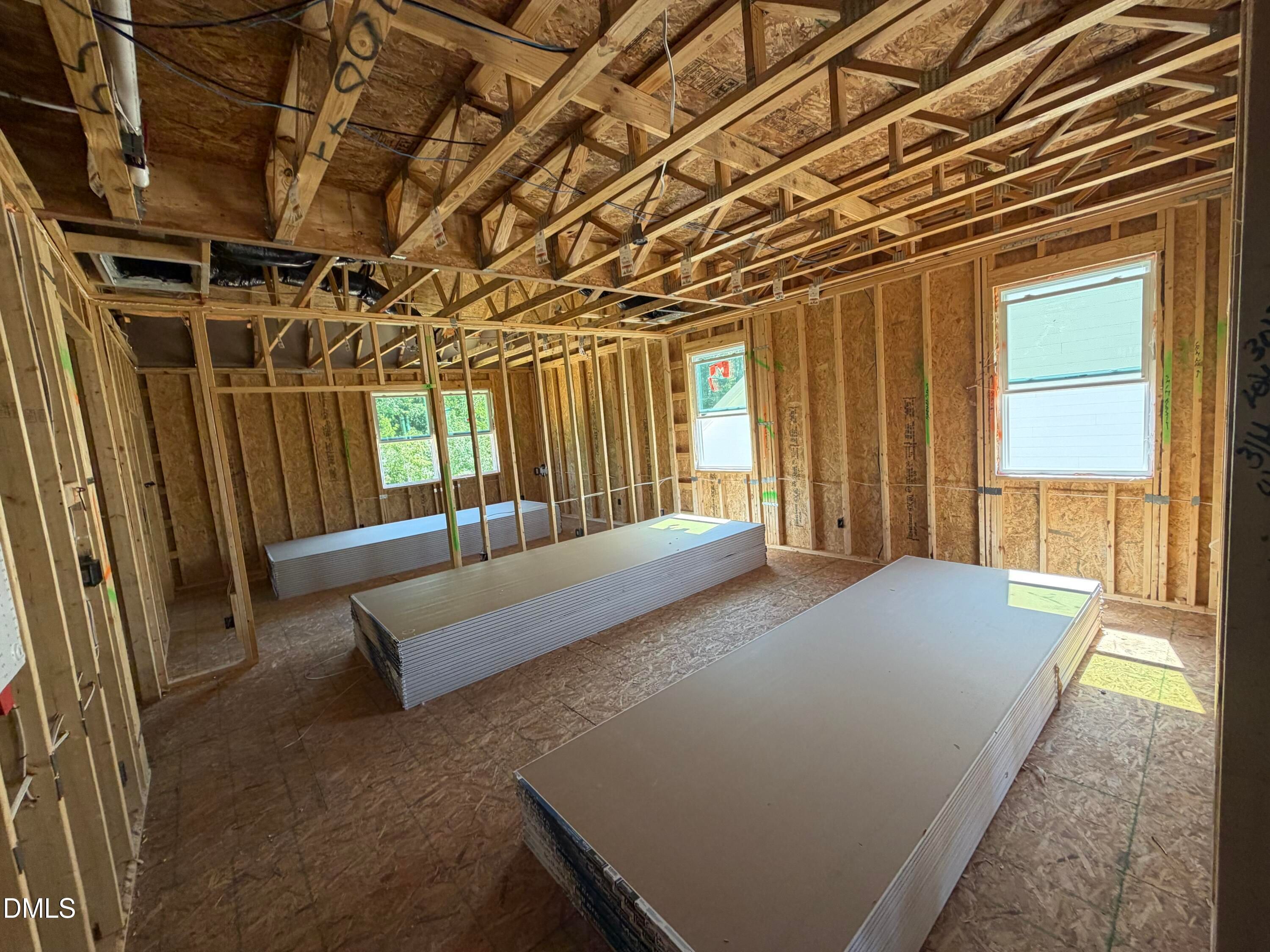 Unfinished framed bonus room with exposed wood trusses and stacked drywall in Davidson Homes The Aspen C, Wendell Ridge, NC