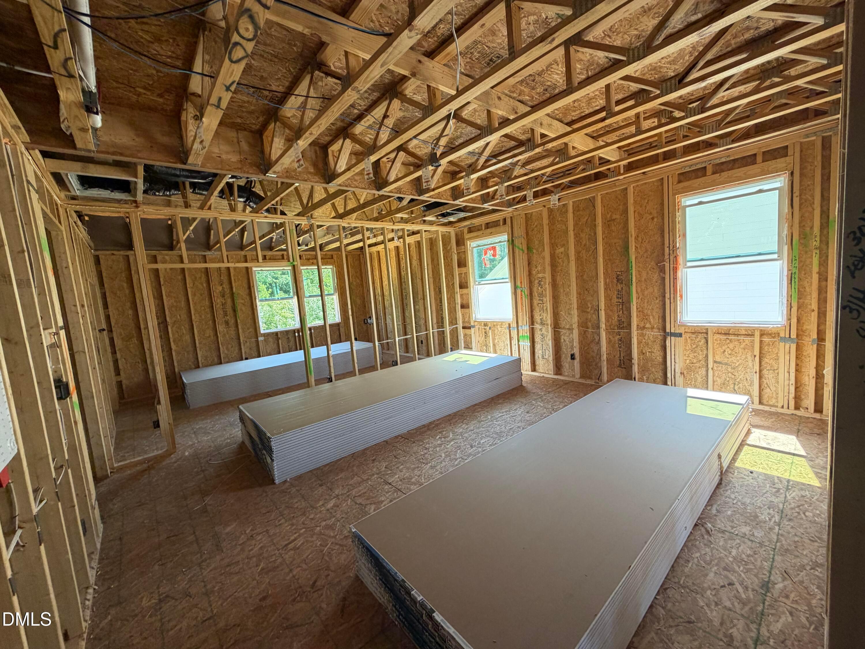 Unfinished framed bonus room with exposed wood trusses and stacked drywall in Davidson Homes The Aspen C, Wendell Ridge, NC