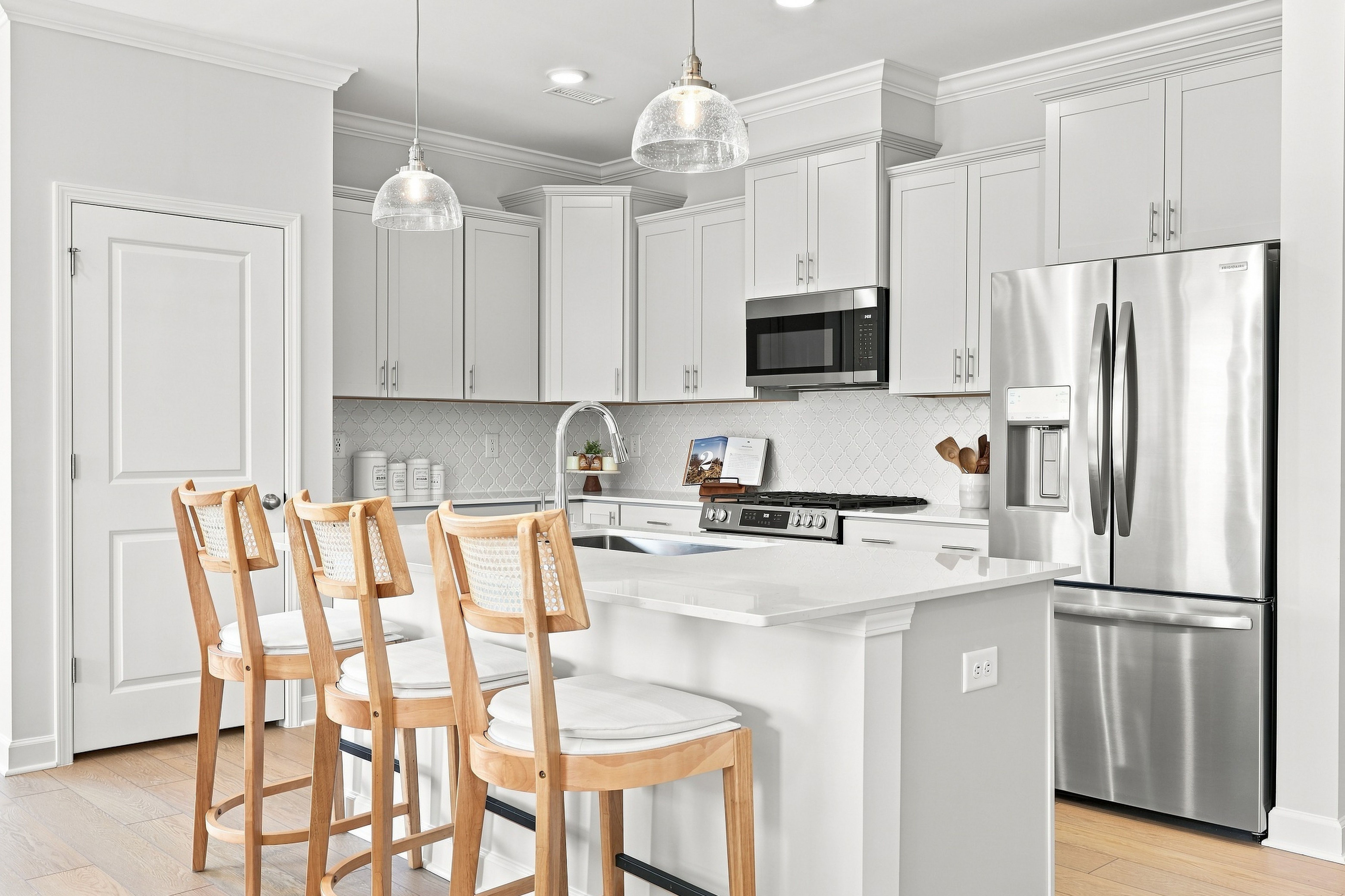 Modern kitchen in The Daphne D featuring white cabinetry, quartz countertops, stainless steel appliances, and a breakfast bar.