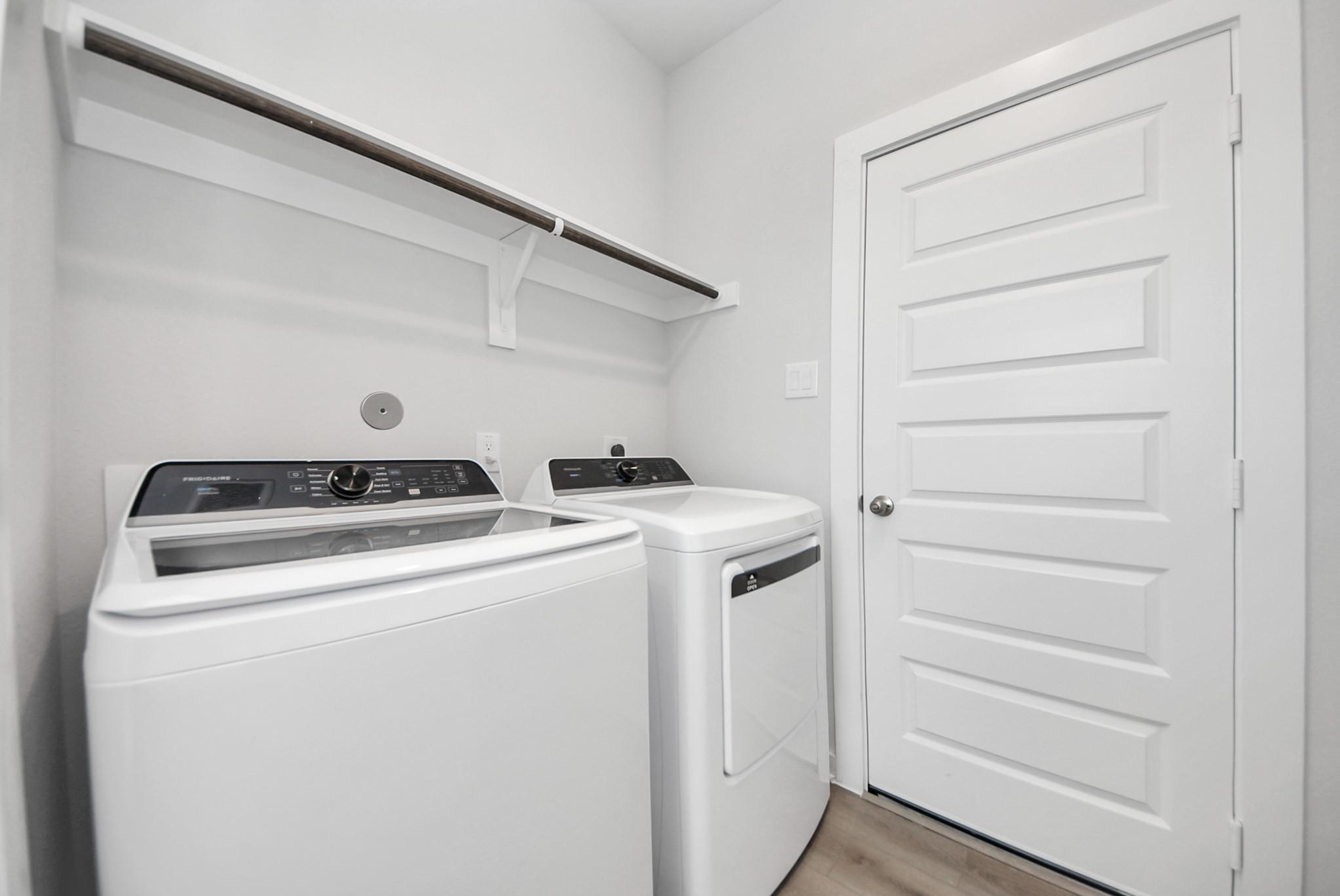Bright utility room with white washer and dryer, hanging rod, and storage shelf in Davidson Homes The San Marcos E, Beasley, Texas