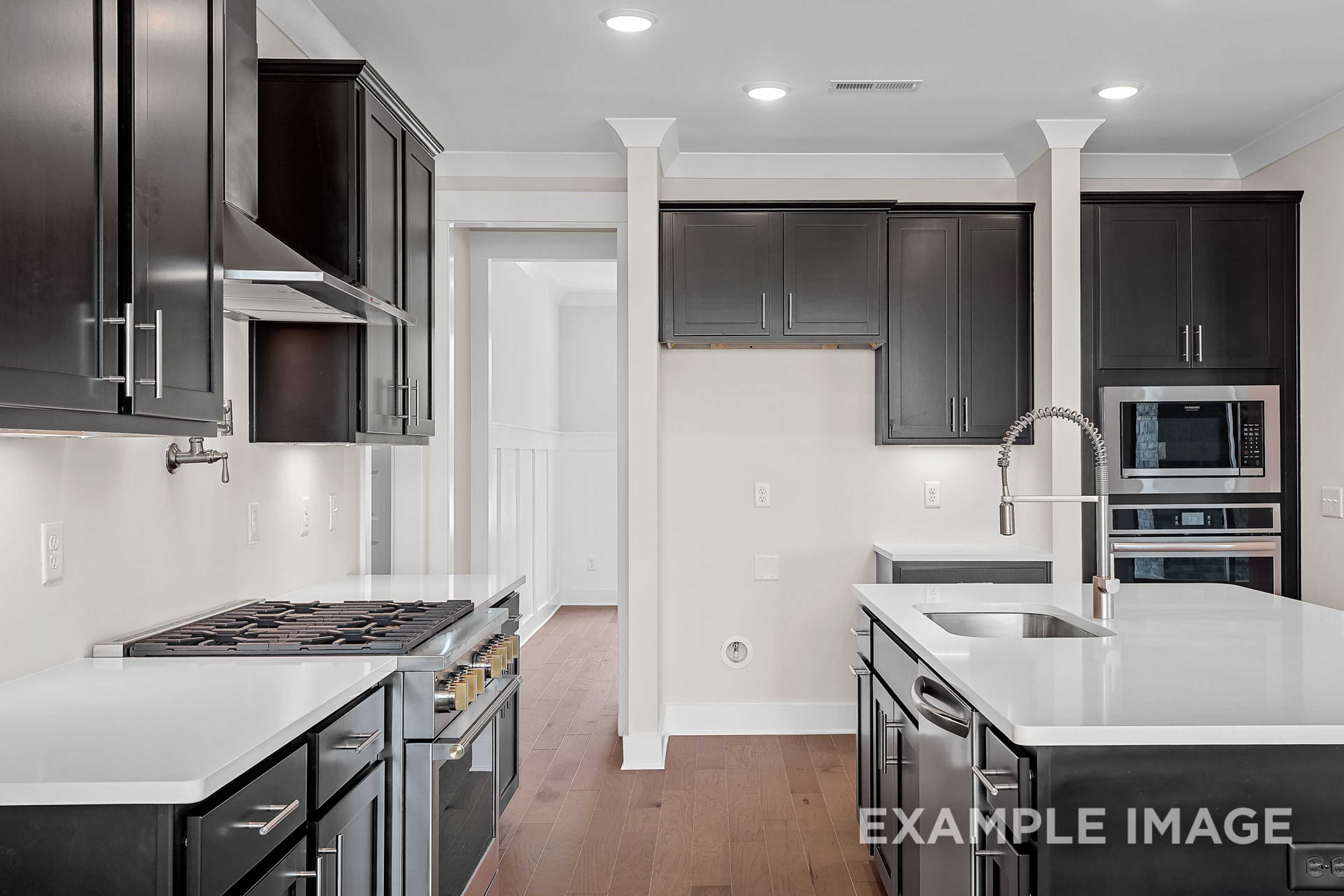 Spacious Hawkins kitchen by Davidson Homes featuring dark cabinetry, white quartz island, gas range, and double ovens
