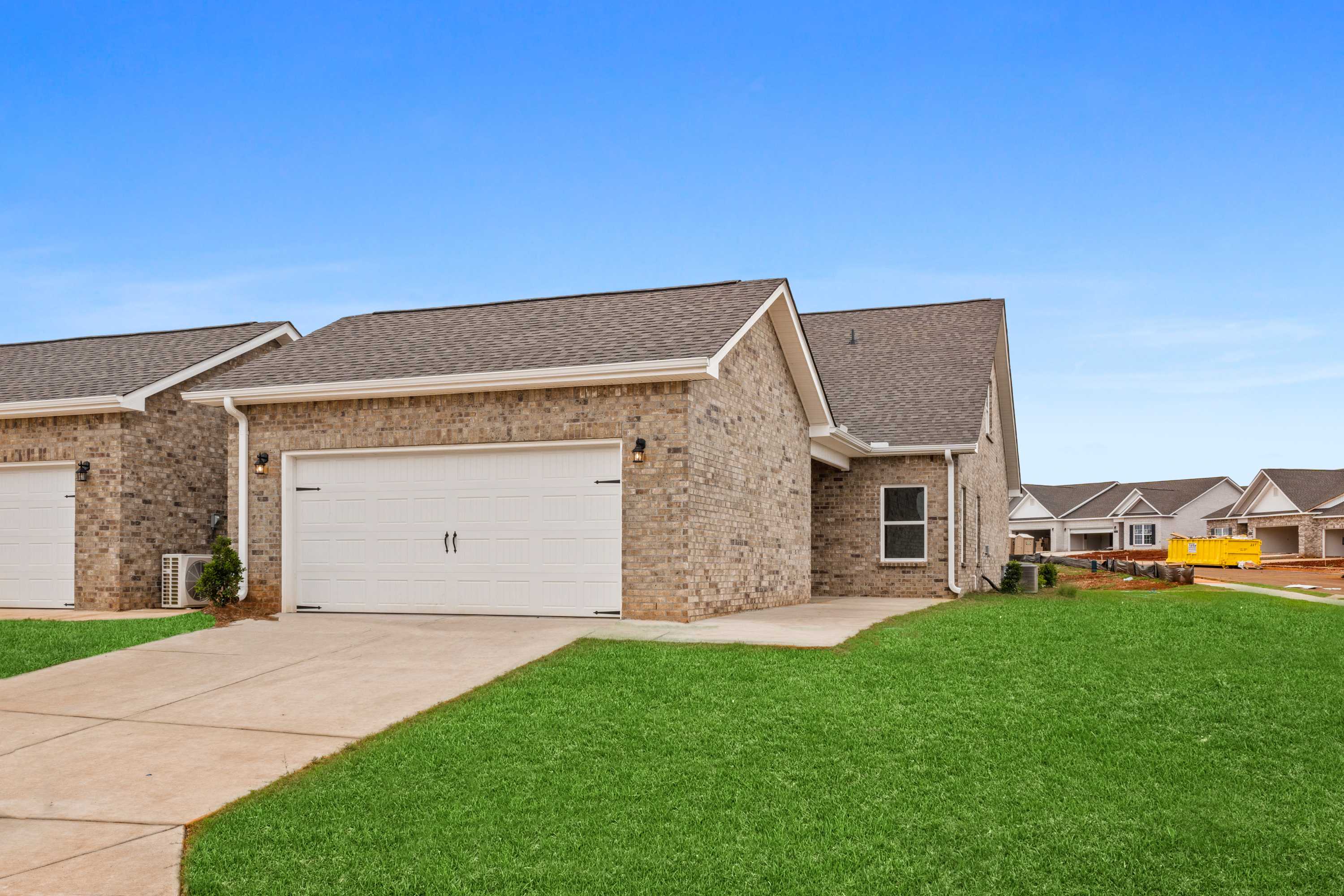Modern stone and siding exterior of The Copeland 2-story multi-family home with 2-car garage, driveway, and lush green lawn in Madison, Alabama