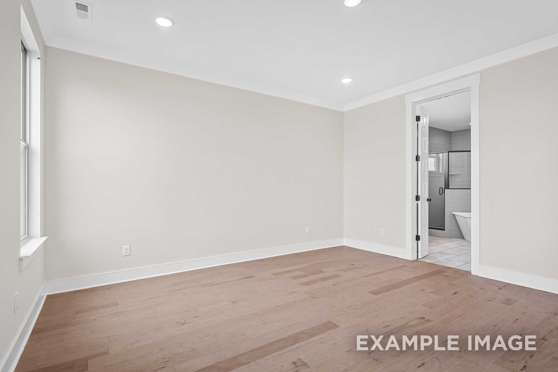 Spacious master bedroom in The Hawkins featuring beige walls, hardwood floors, and en-suite bathroom with freestanding tub