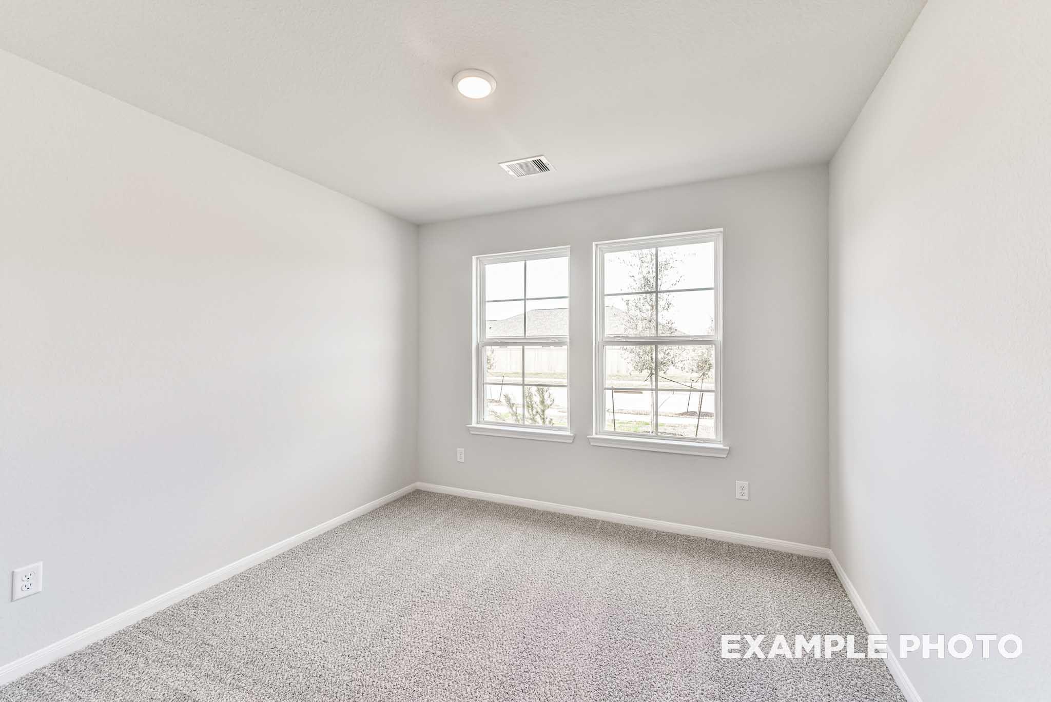 Bright, neutral bedroom with plush carpet and two windows in The Laguna C floor plan at Sunterra in Katy, Texas.