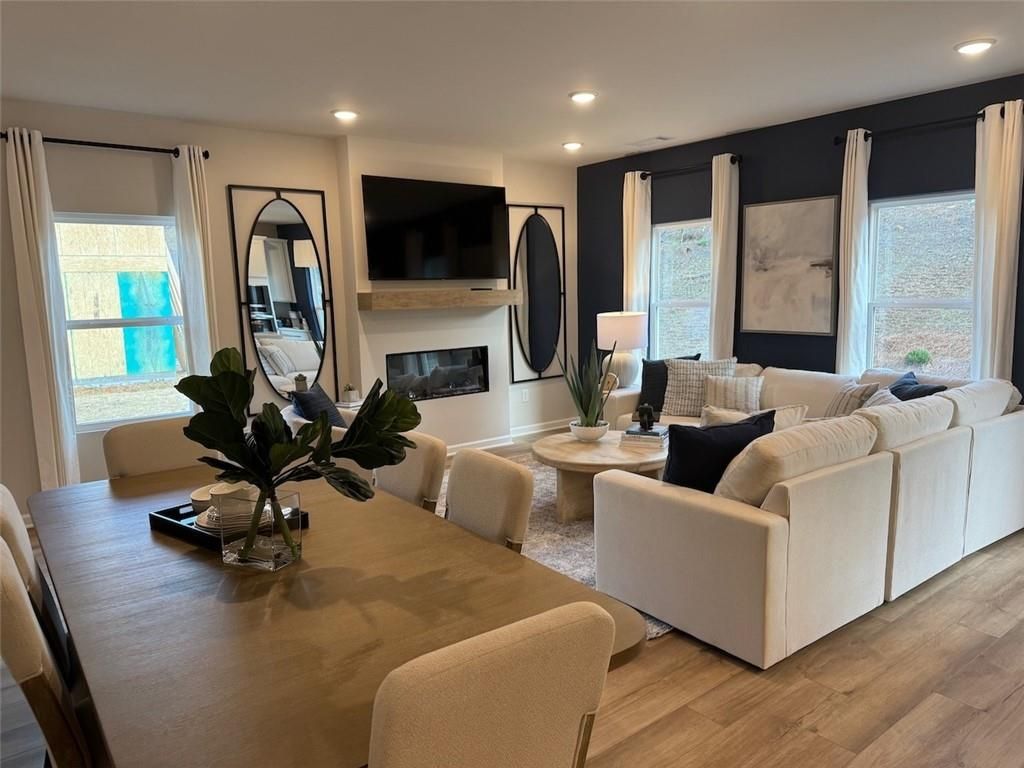 Modern open-concept living room with white sectional sofa, gas fireplace, dining table, and large mirrors in Davidson Homes The Hartwell A, Canton, GA