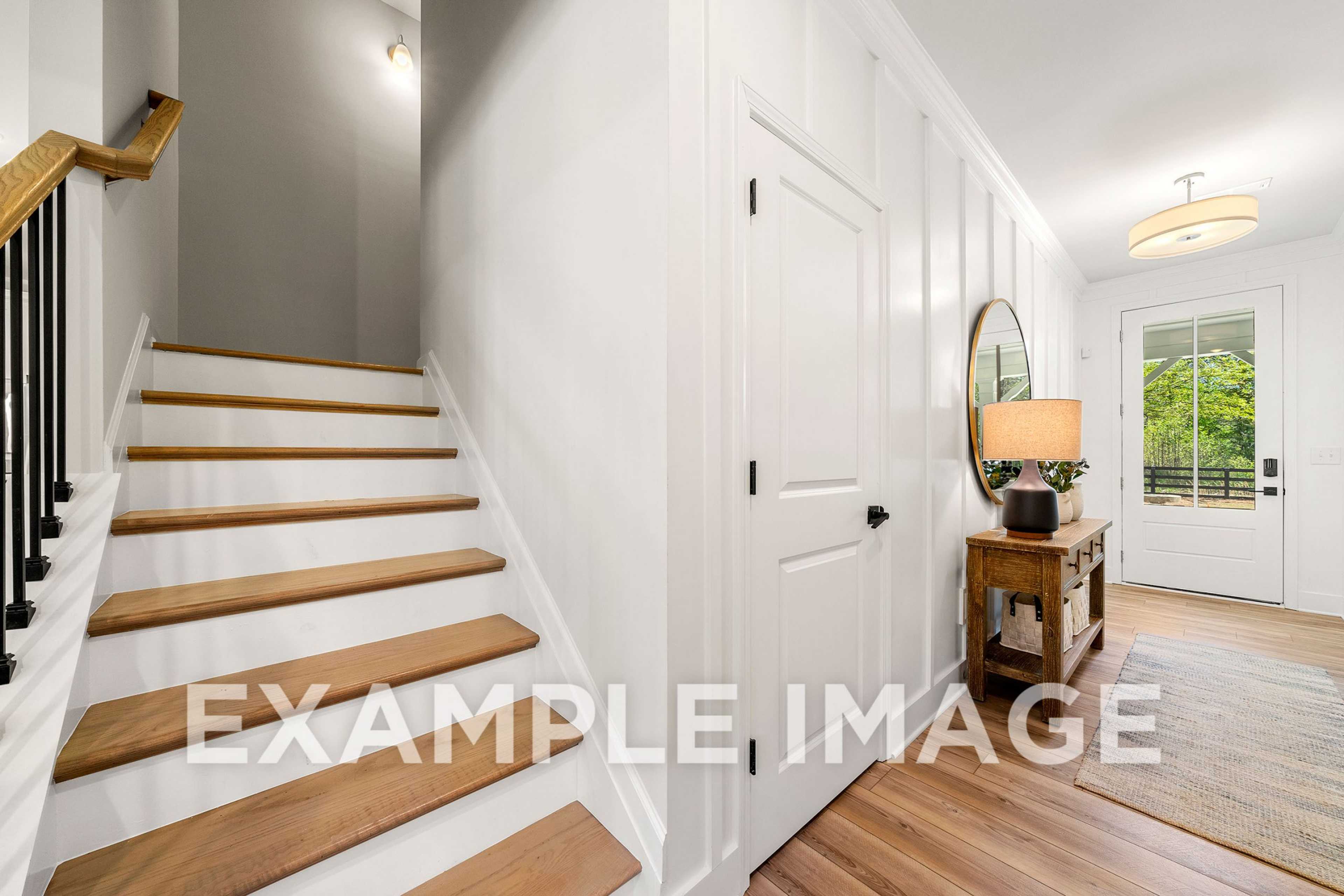 Bright entryway of The Hickory A home with oak staircase, white shiplap walls, console table, and front door