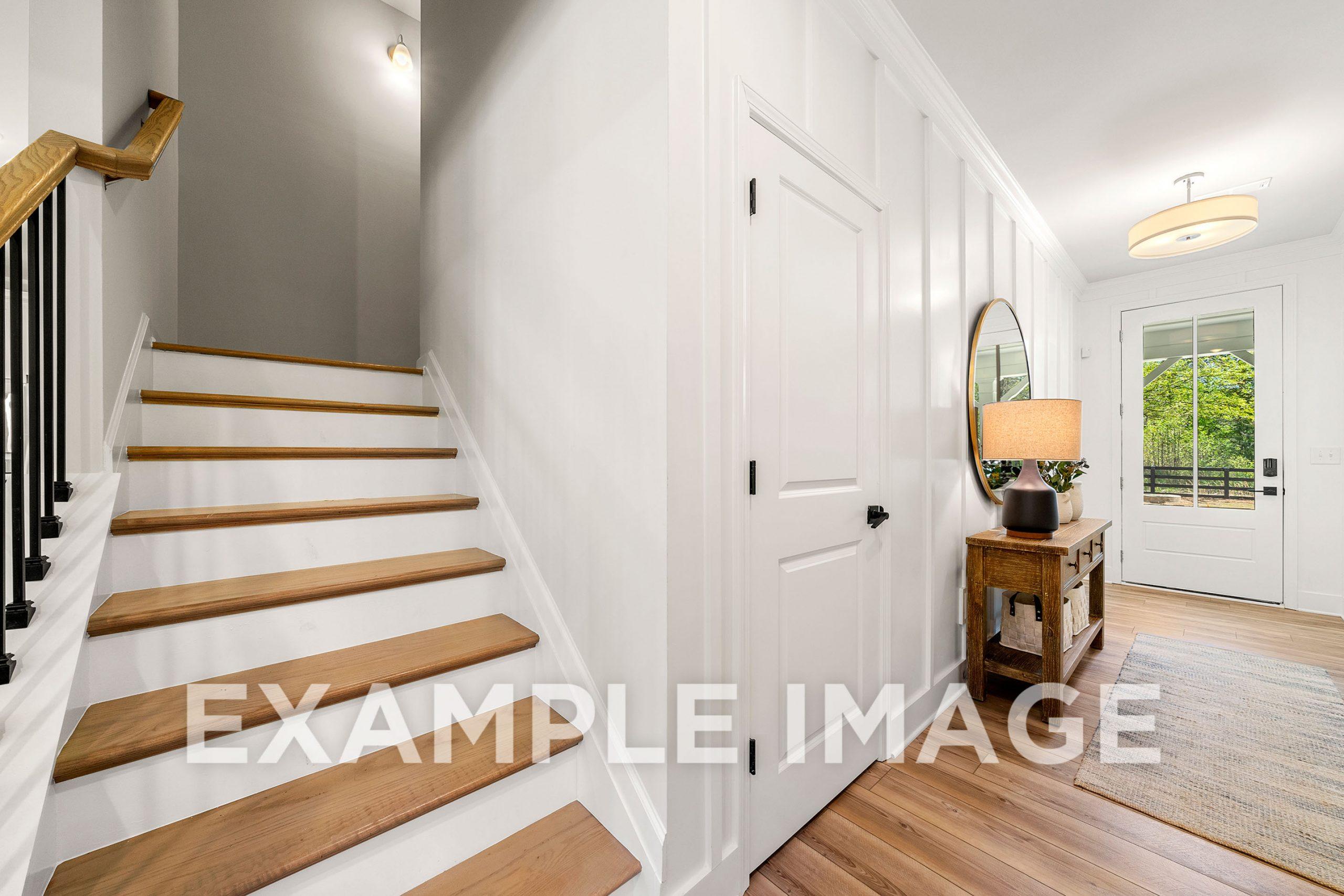 Bright entryway in The Hickory B home featuring oak staircase, white board-and-batten walls, console table with lamp