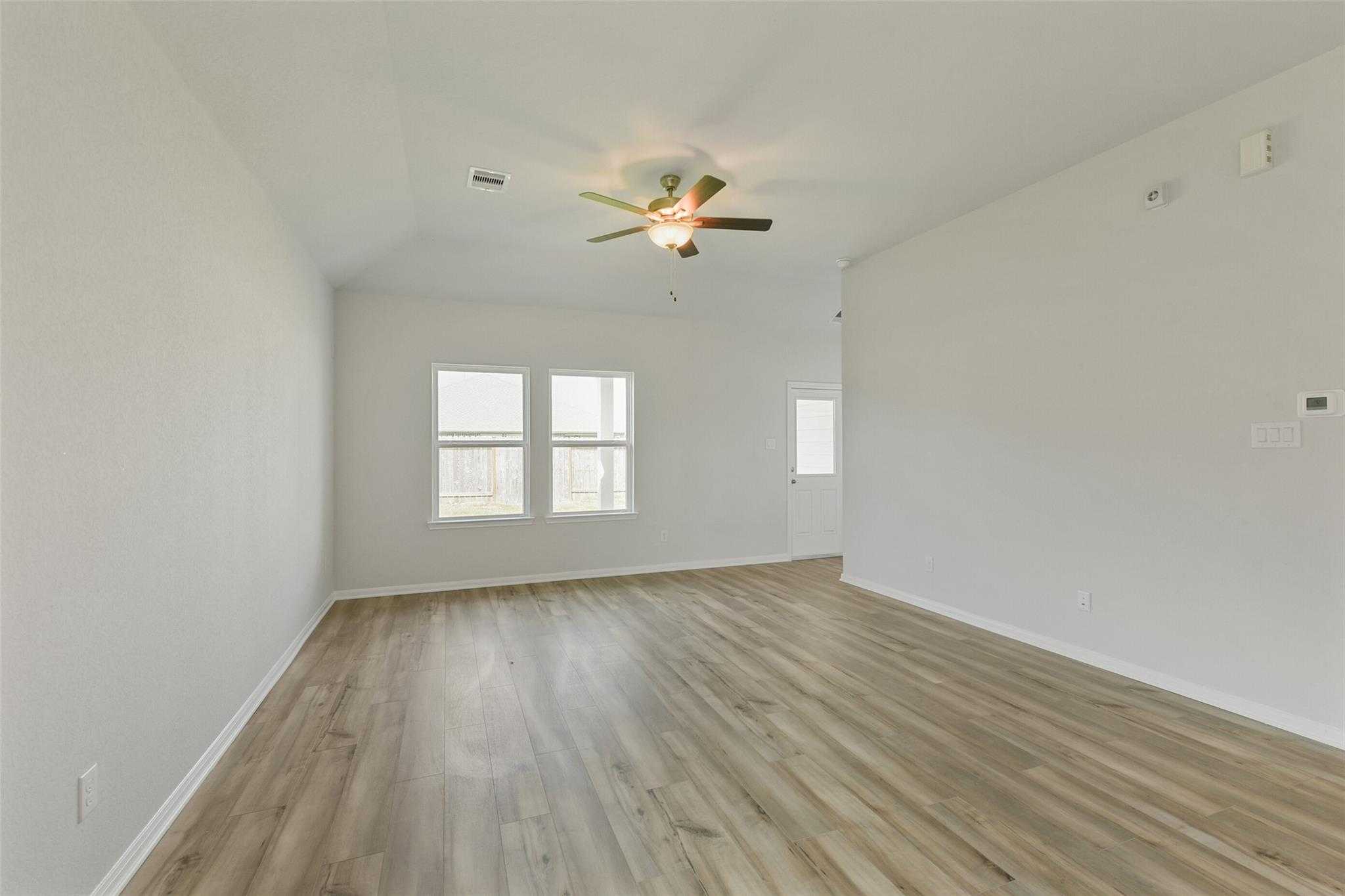 Spacious living room with laminate wood floors, ceiling fan, and large double windows in The Laguna B home, Dayton Texas