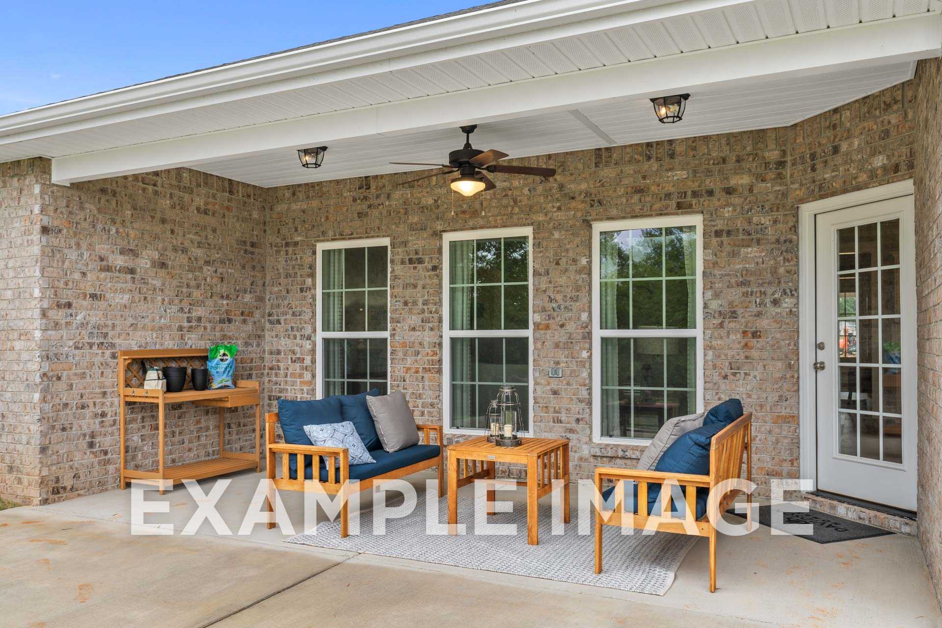 Spacious covered patio of The Harrison B showcasing brick exterior, large windows, wooden furniture, ceiling fan, Meridianville home