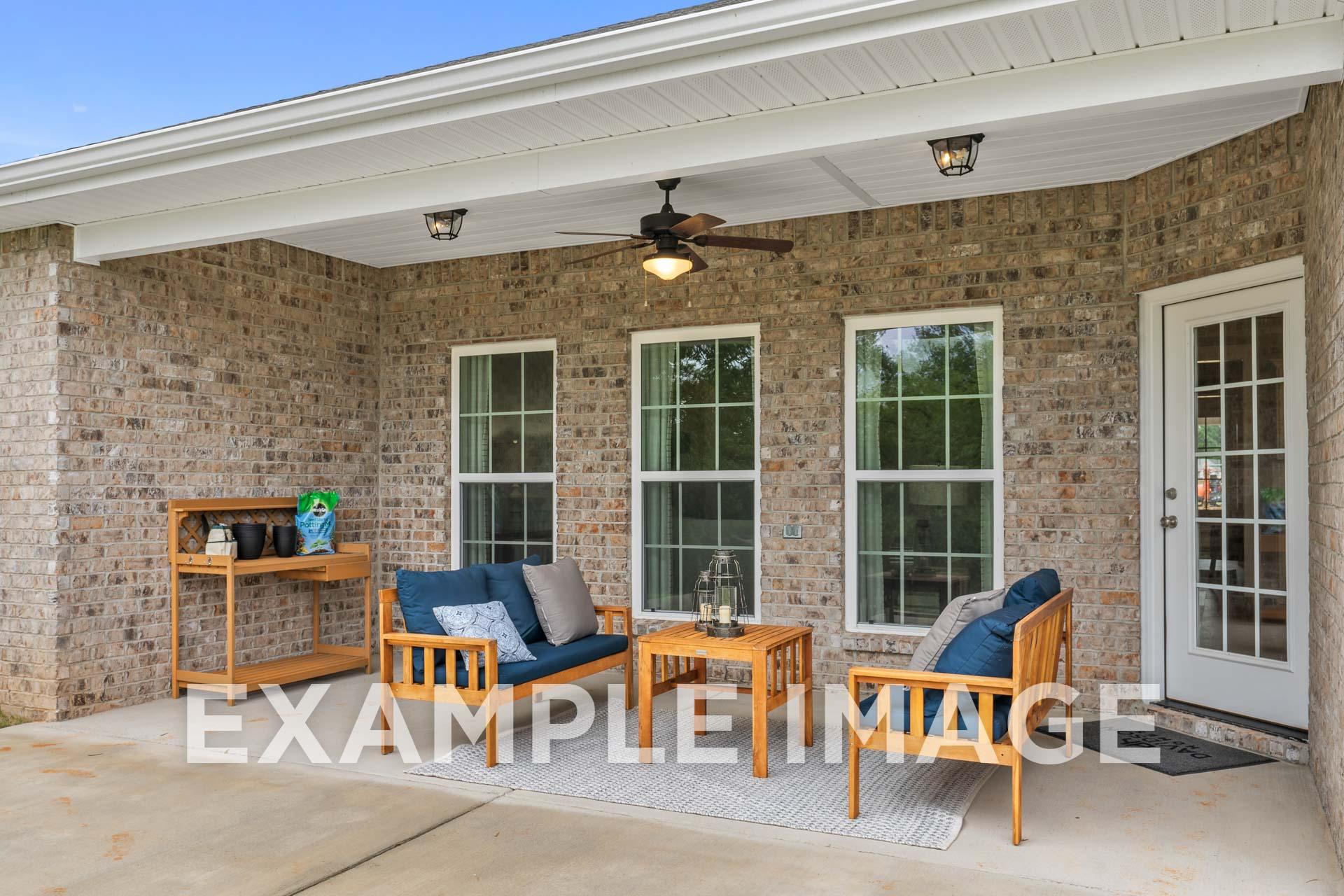 Spacious covered patio of The Harrison B showcasing brick exterior, large windows, wooden furniture, ceiling fan, Meridianville home